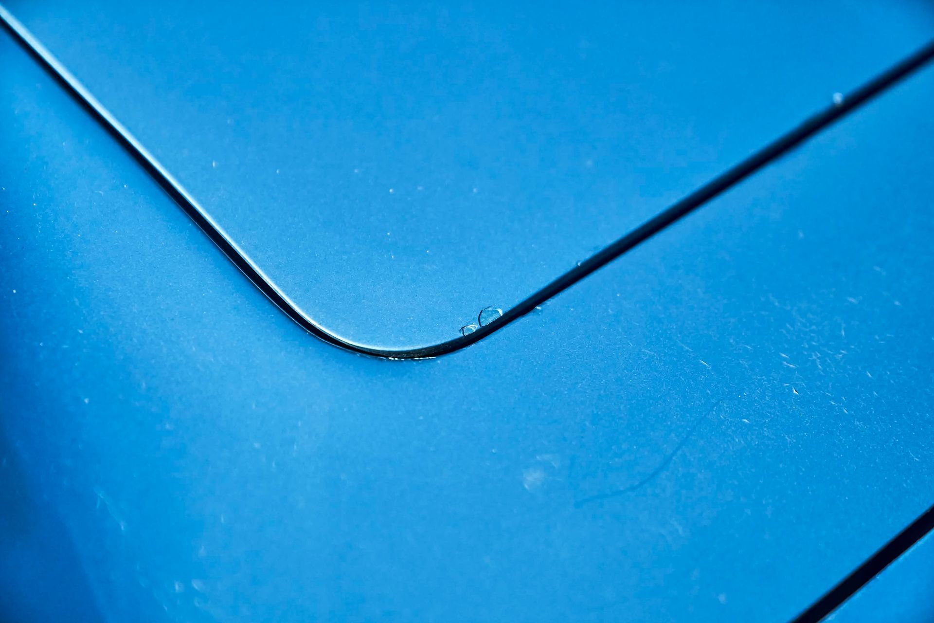 Close-up of a light blue surface with a curved black line, possibly part of a car.