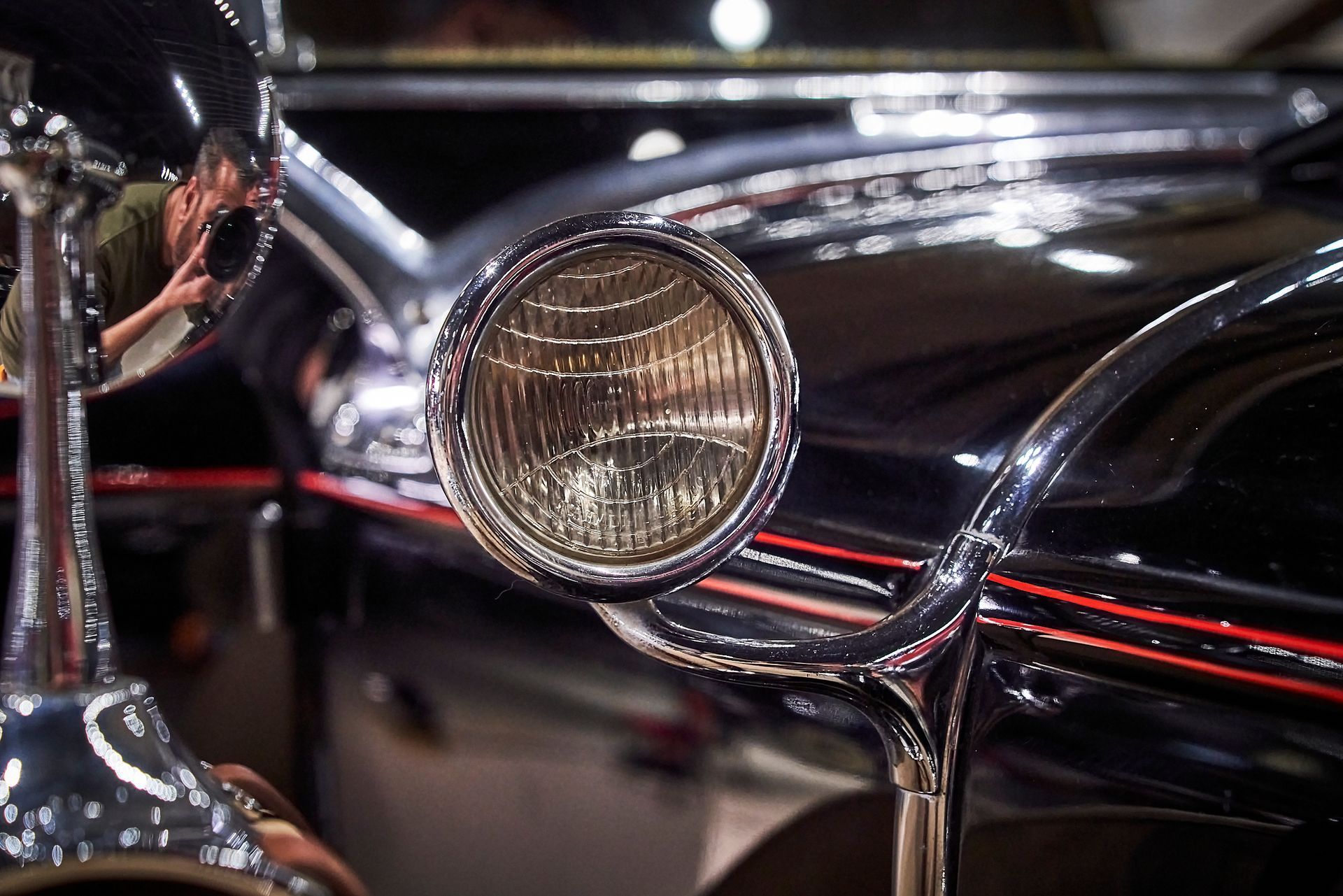 A close up of a car headlight with a reflection of a person in the mirror.