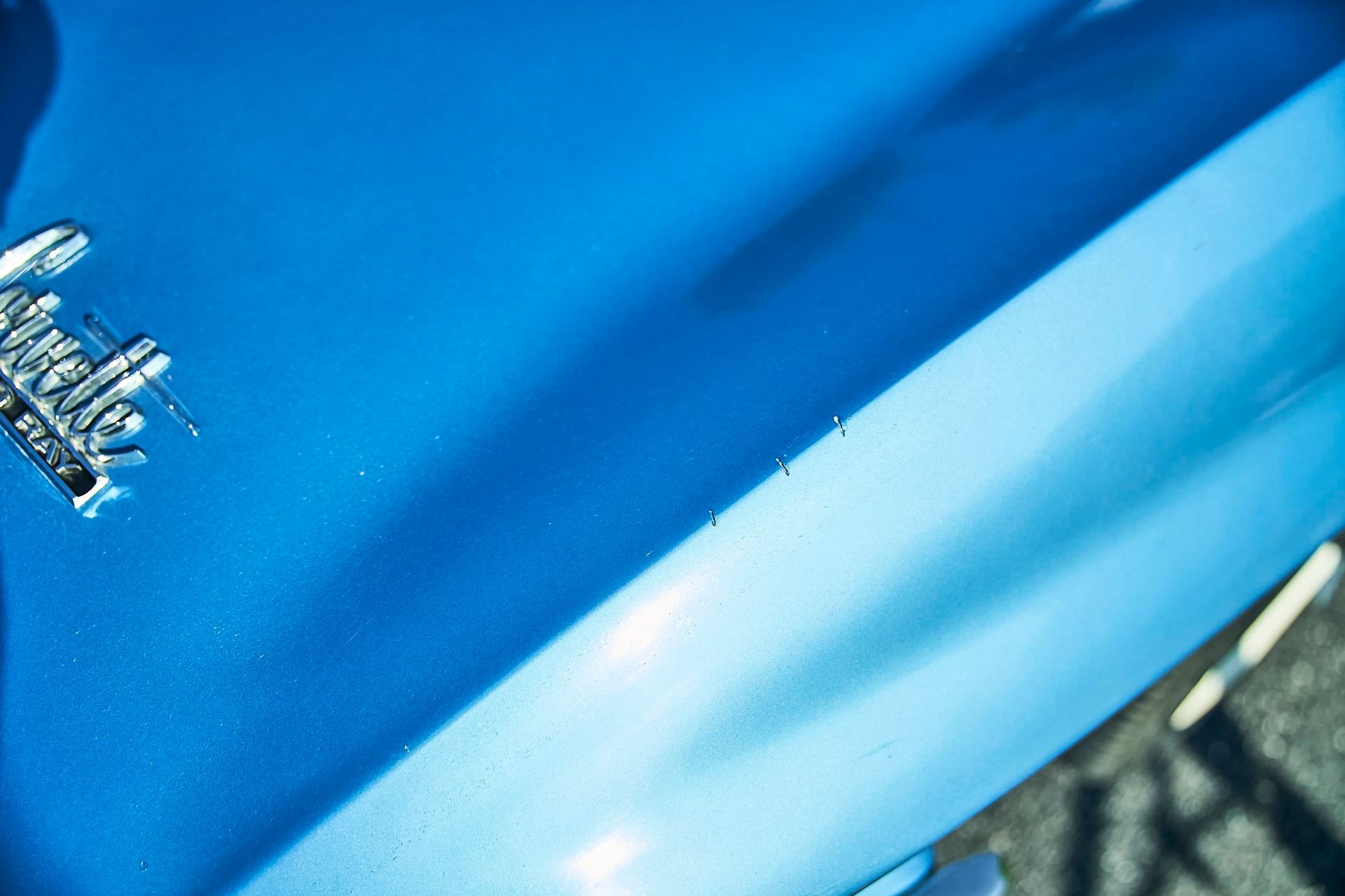 Close-up of a bright blue car's body with a silver emblem, showcasing a shiny, detailed surface.