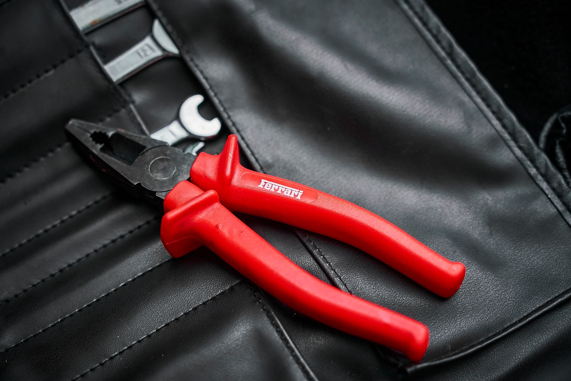 A pair of red pliers is sitting on top of a black leather bag.