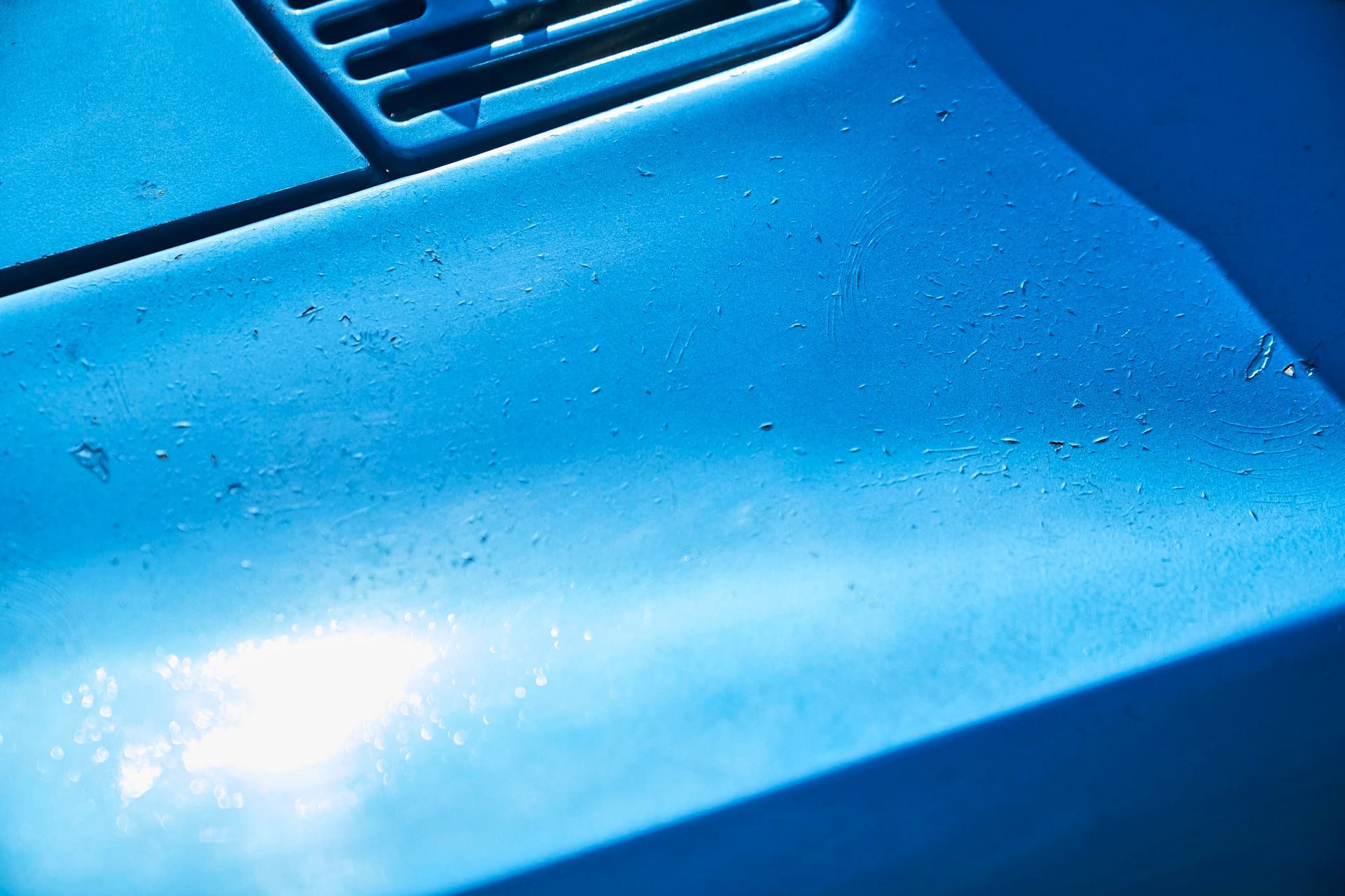 Blue car hood with water droplets, reflecting sunlight.