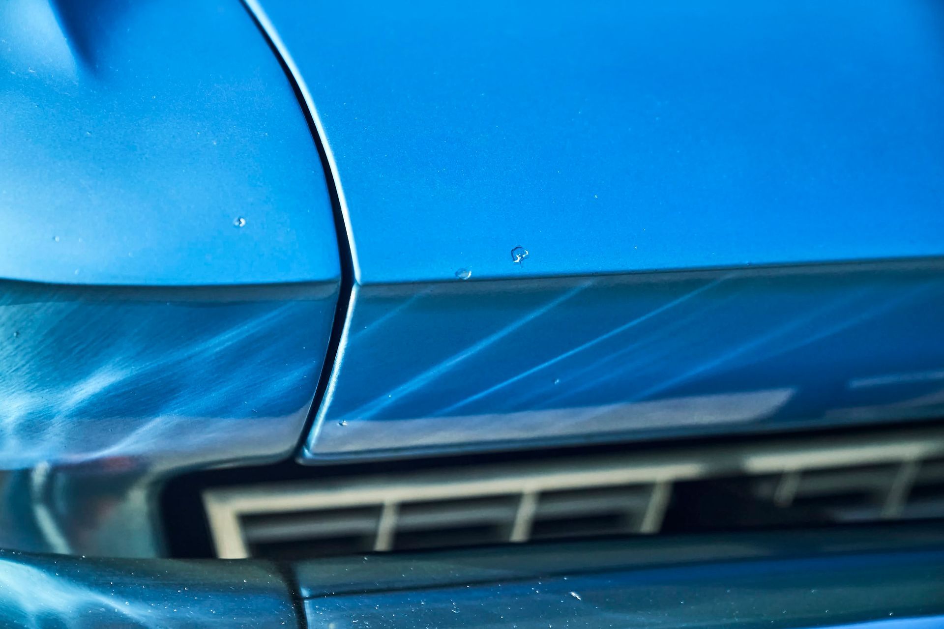 Close-up of a blue car's hood with shiny highlights and a vent below.