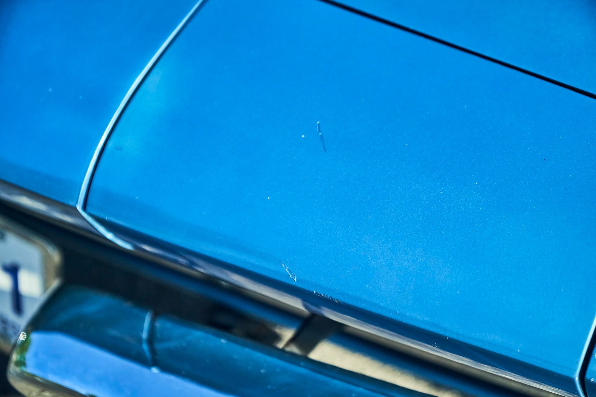 Close-up of a classic blue car's hood, showcasing paint detail and a silver trim.