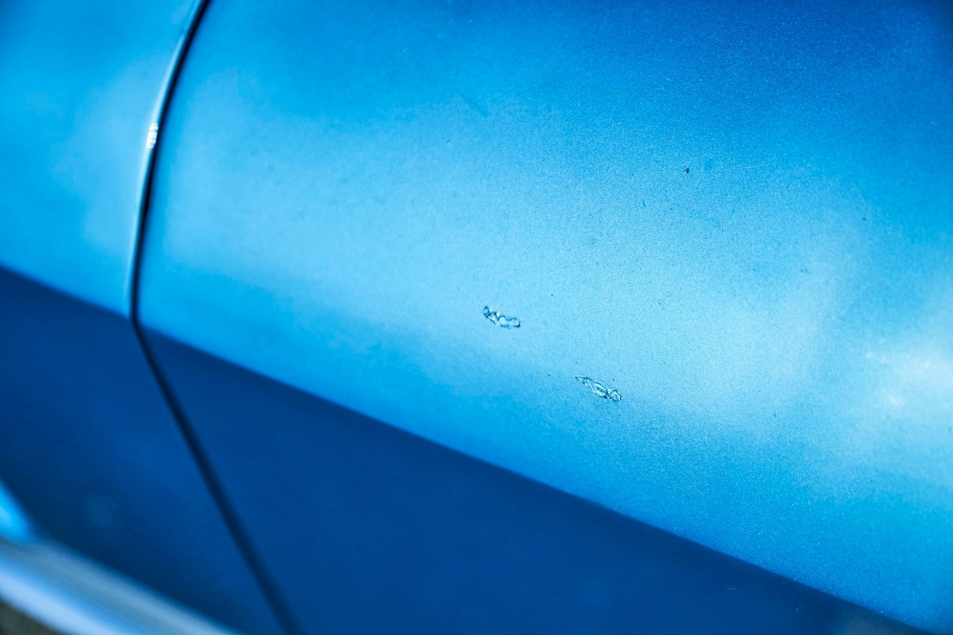 Close-up of blue car paint with small scratches, reflecting light.