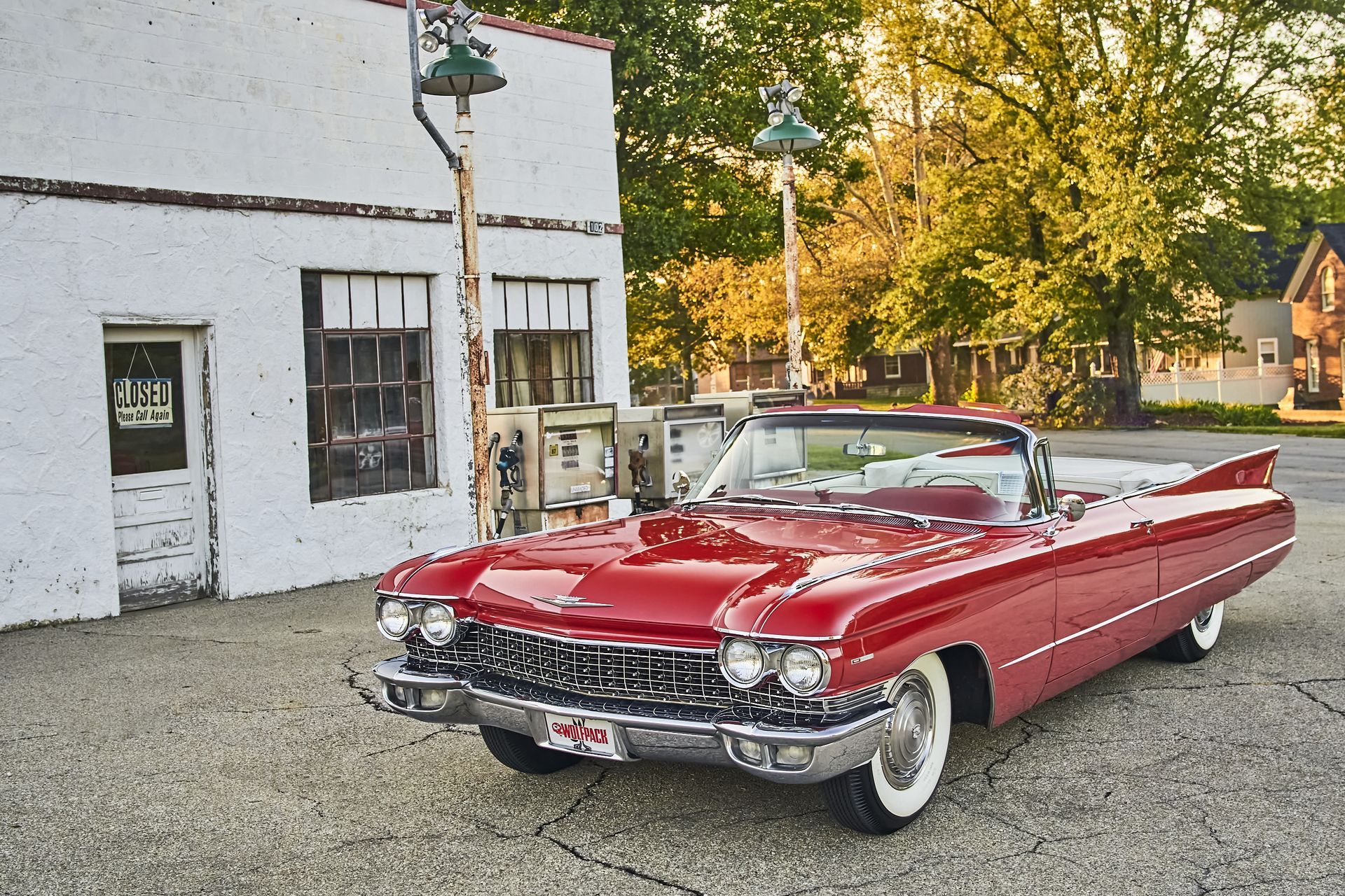 A red cadillac convertible is parked in front of a white building.
