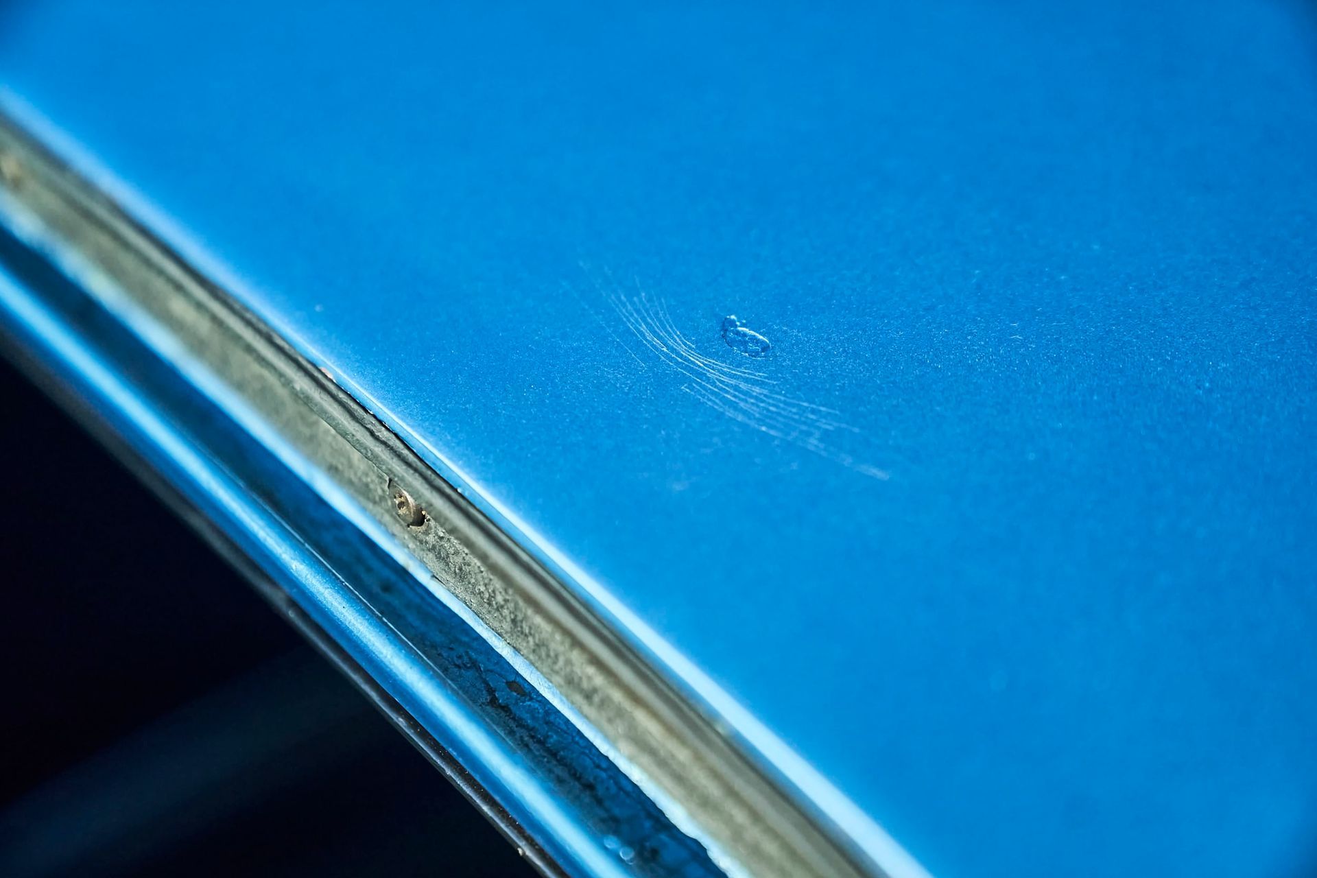 Close-up of a bright blue car surface with minor scratches near a window frame.