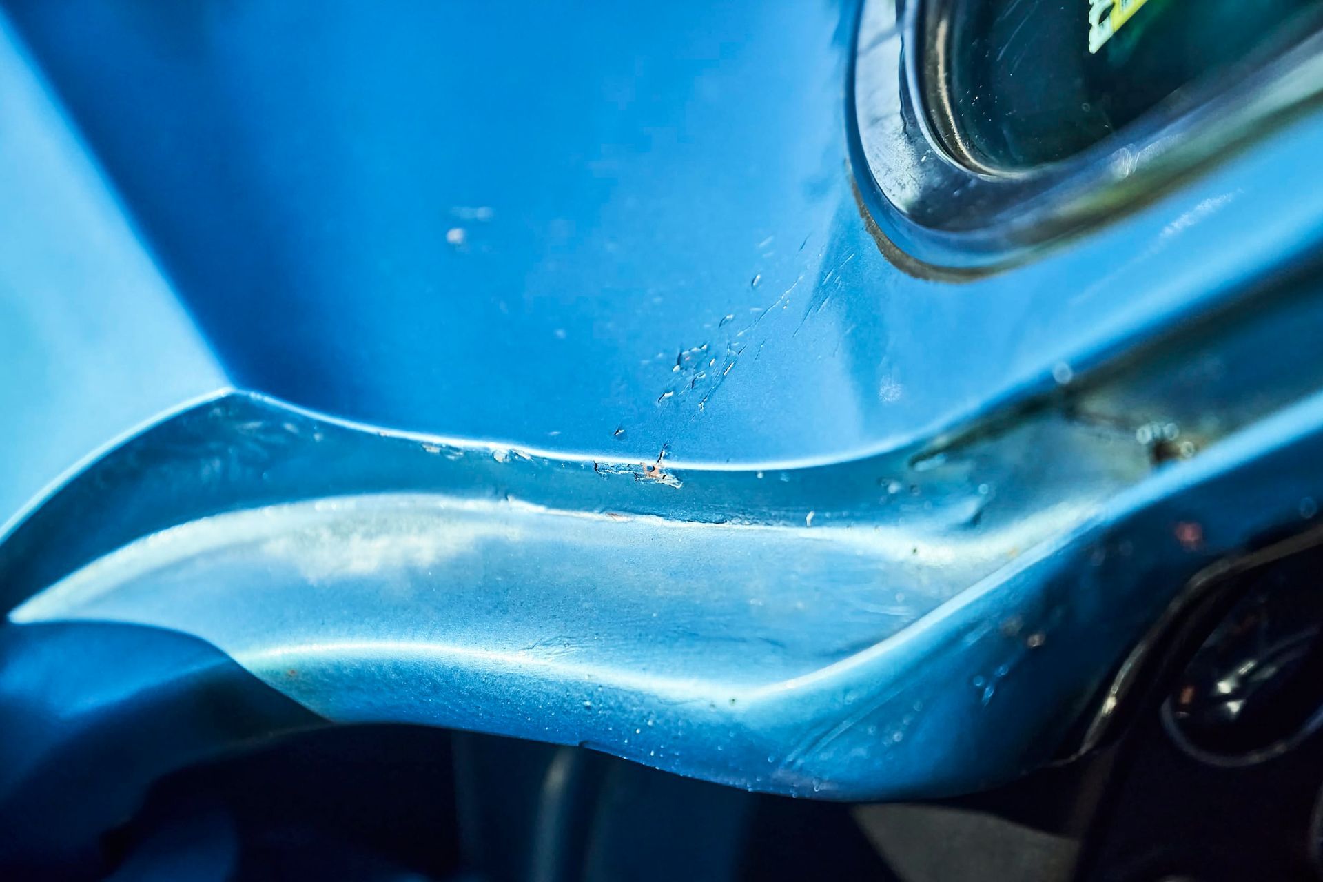 Close-up of a weathered, light blue car dashboard. Shiny, curved sections contrast with textured, faded paint and signs of wear.