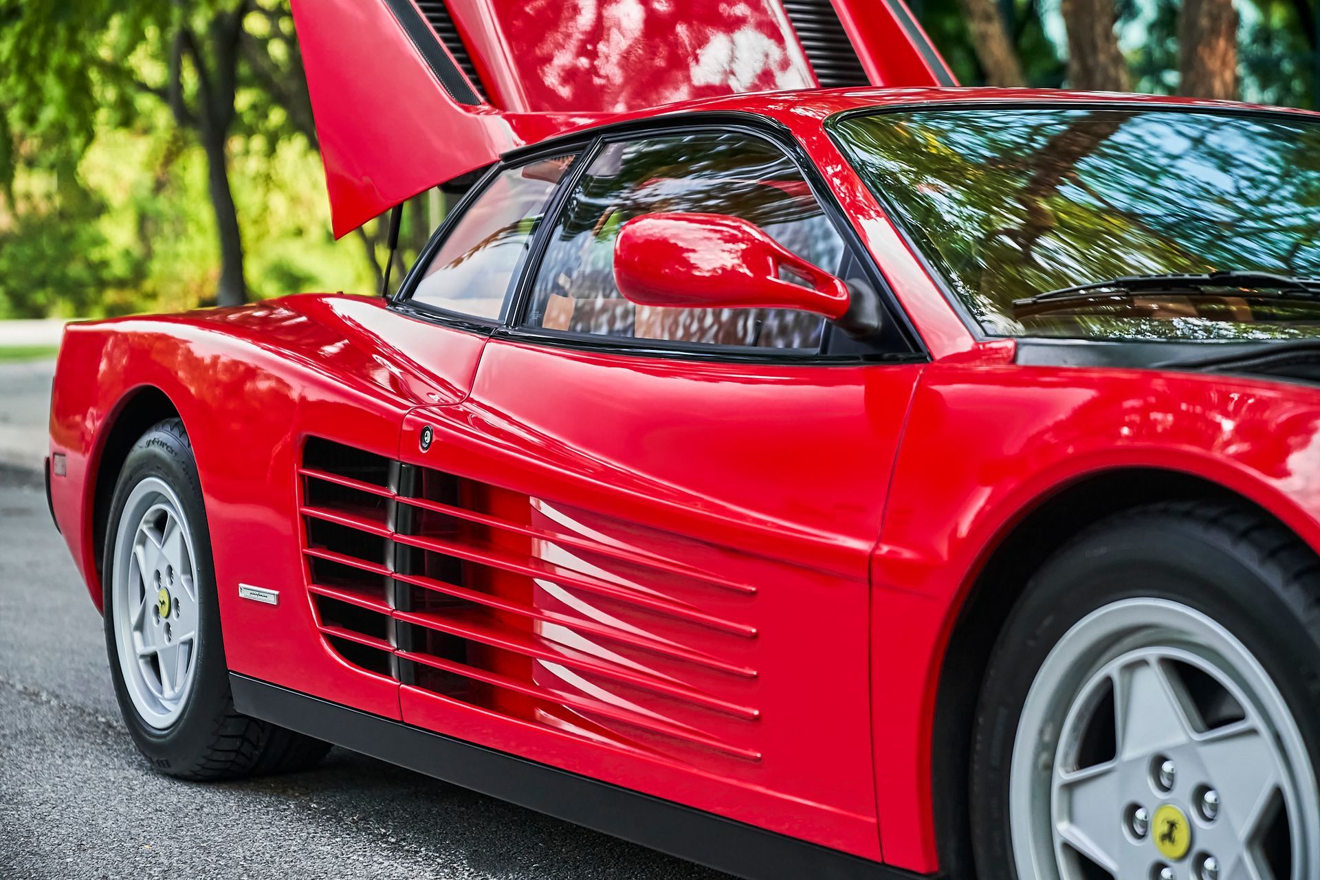 A red ferrari with the hood up is parked on the side of the road.