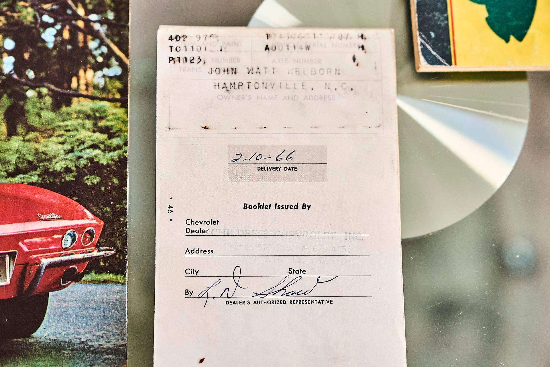 Document with handwritten text, a book cover with a red car, and a reflective disc.