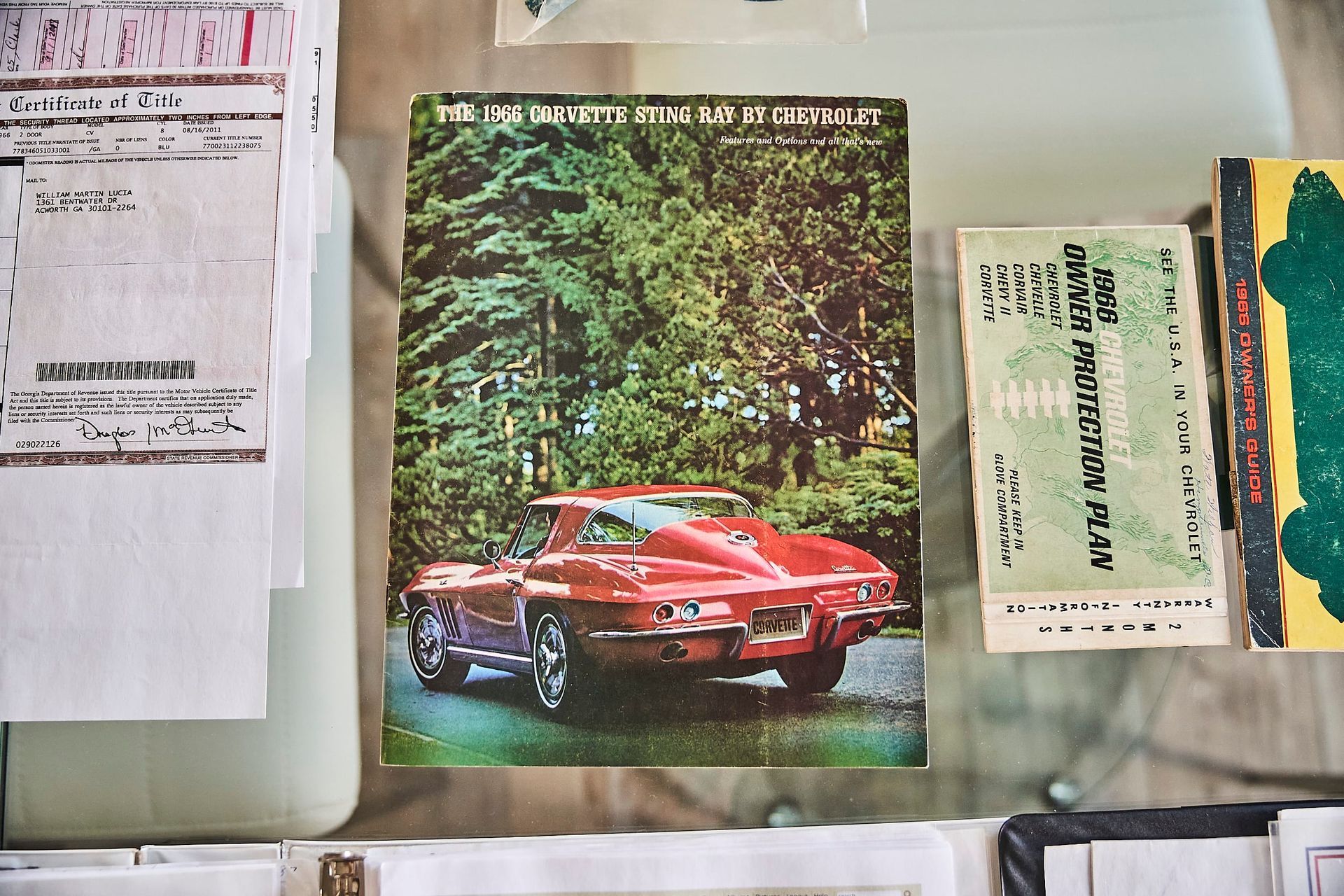A magazine with a red Corvette on the cover sits on a glass surface, surrounded by papers and other magazines.