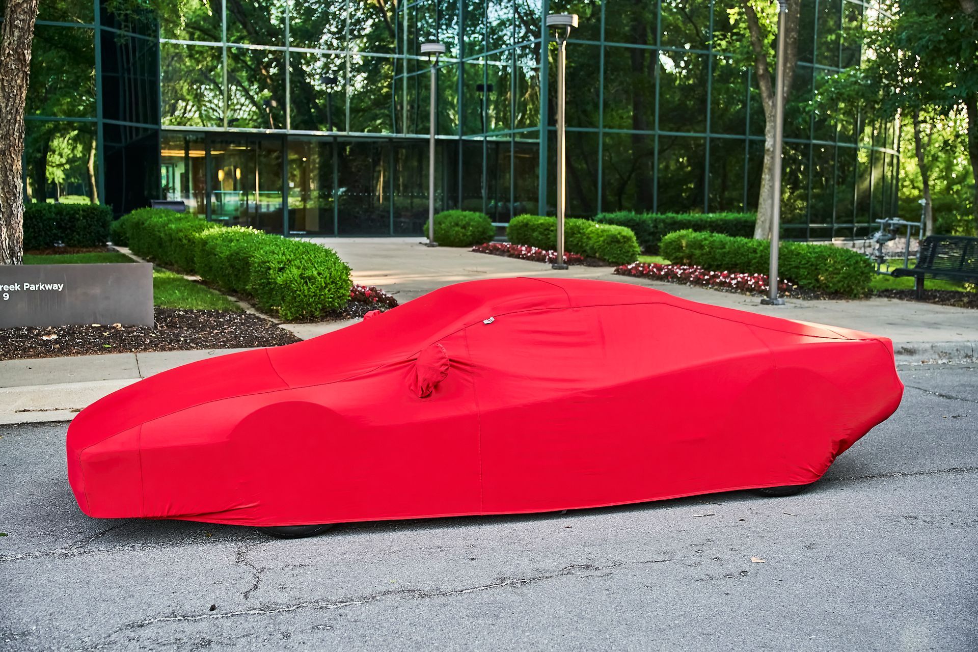 A red car is covered in a red cover in front of a building