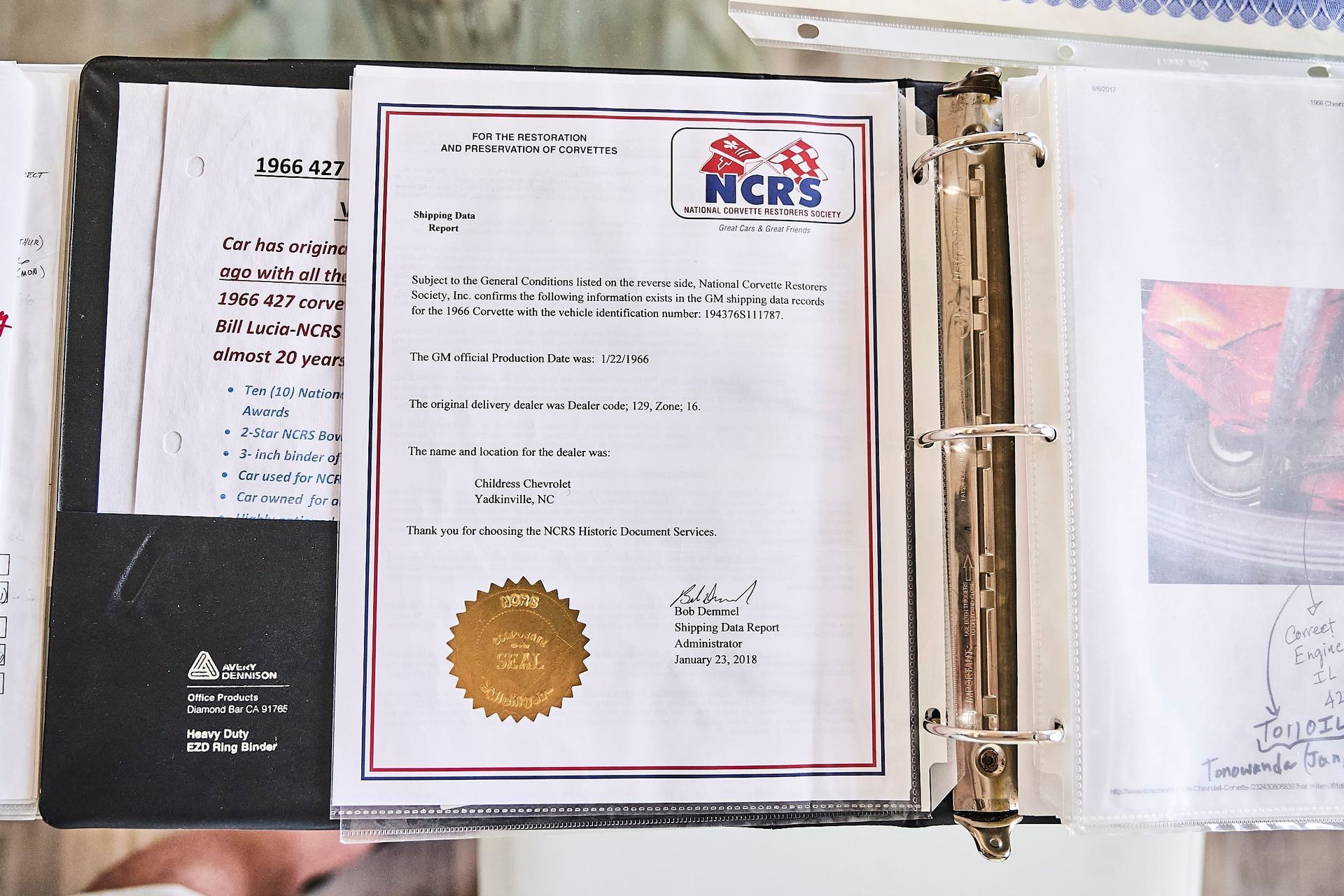 Open binder with documents, including a certificate with a gold seal, and handwritten notes.