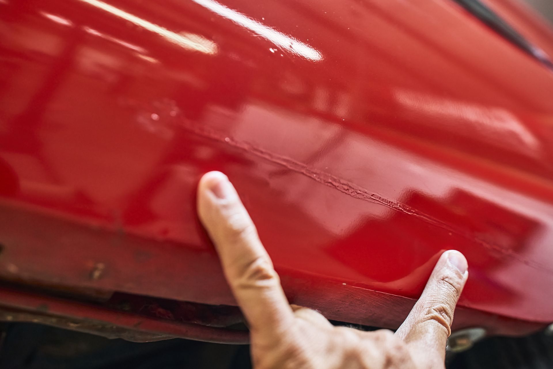 A person is pointing at a scratch on the side of a red car.