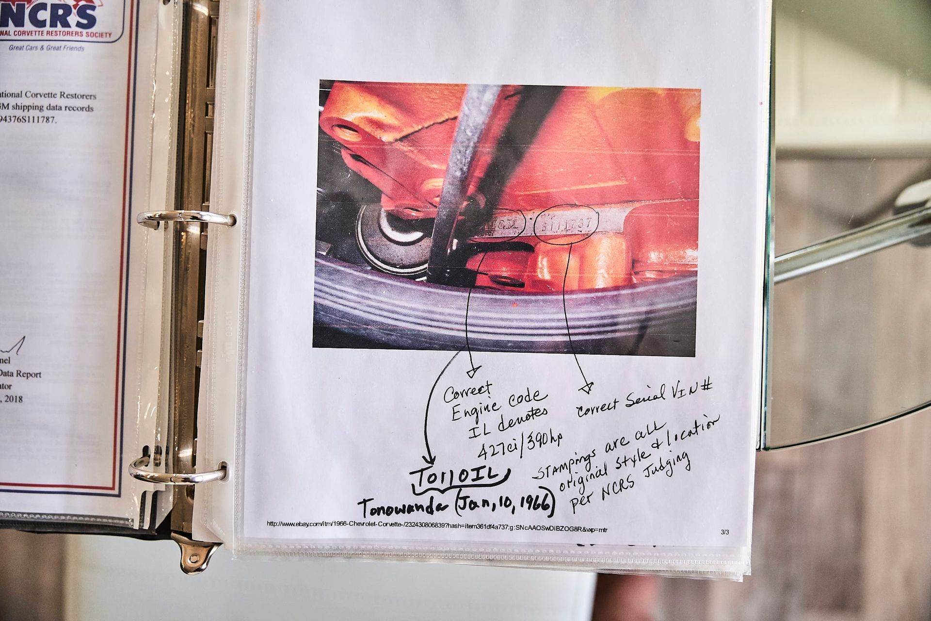 Close-up of a torn image on a binder page, with handwritten notes pointing out car parts like engine and lower frame elements.