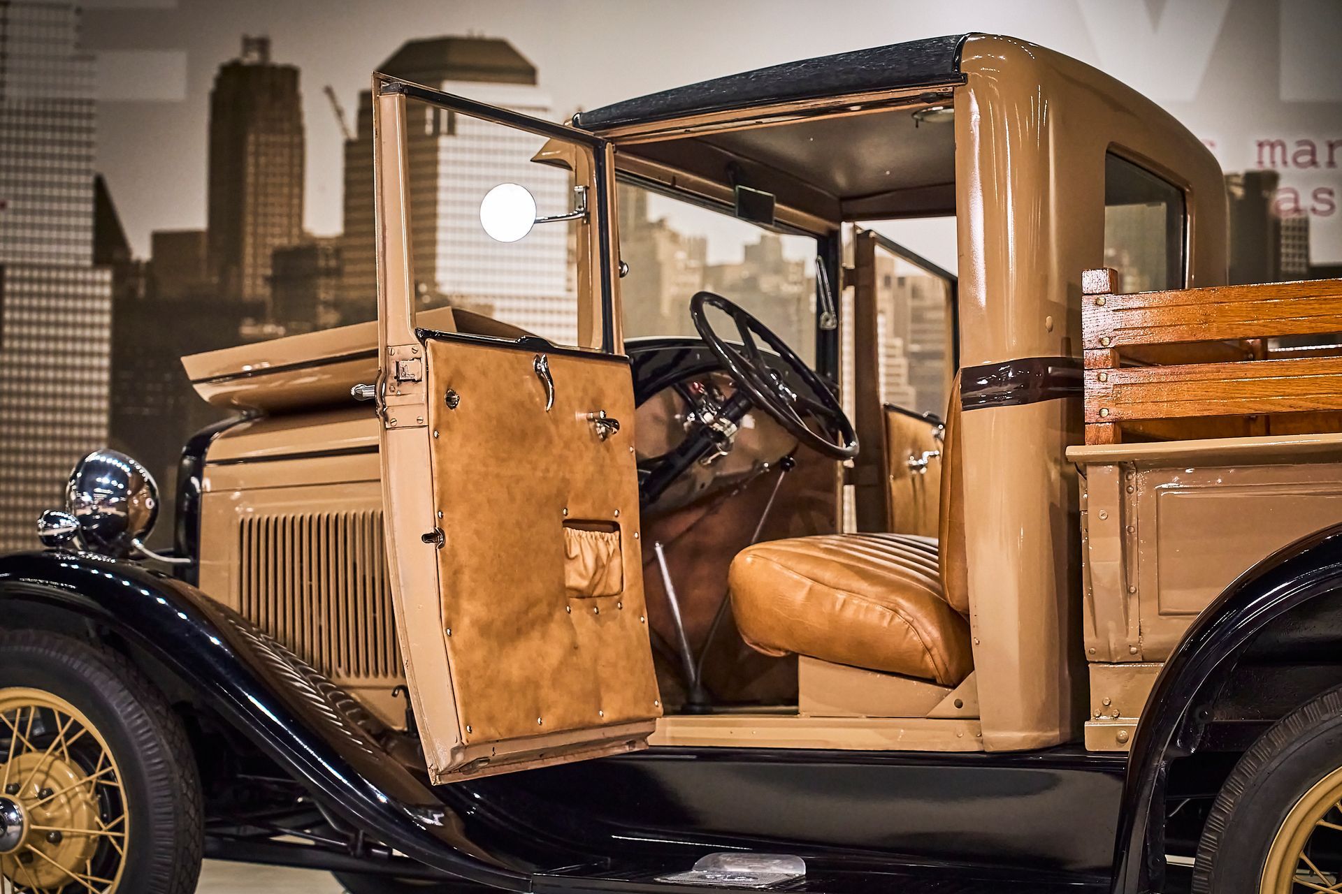 An old truck with the door open is parked in front of a city skyline.