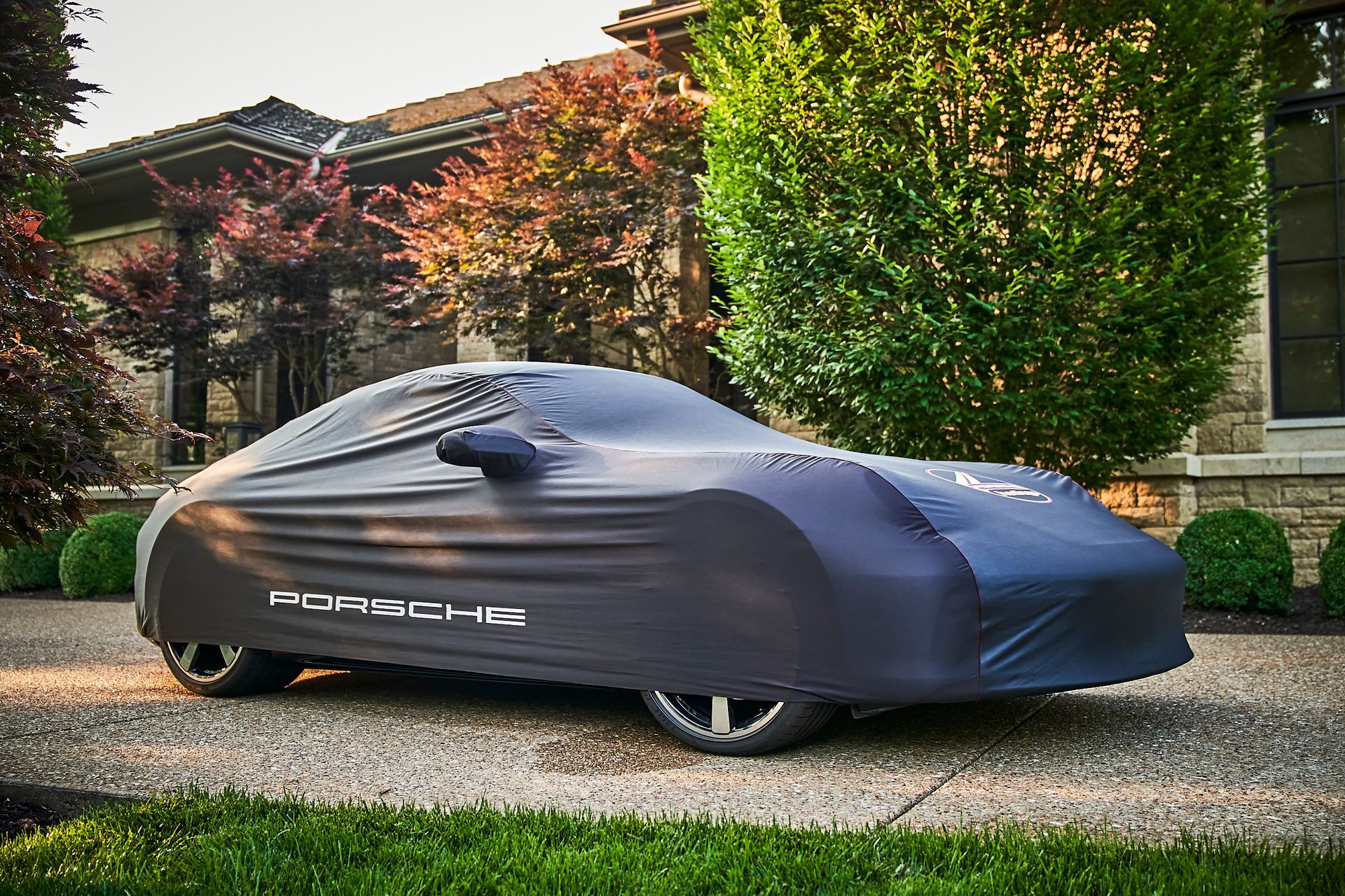 A porsche is covered in a car cover and parked in front of a house.
