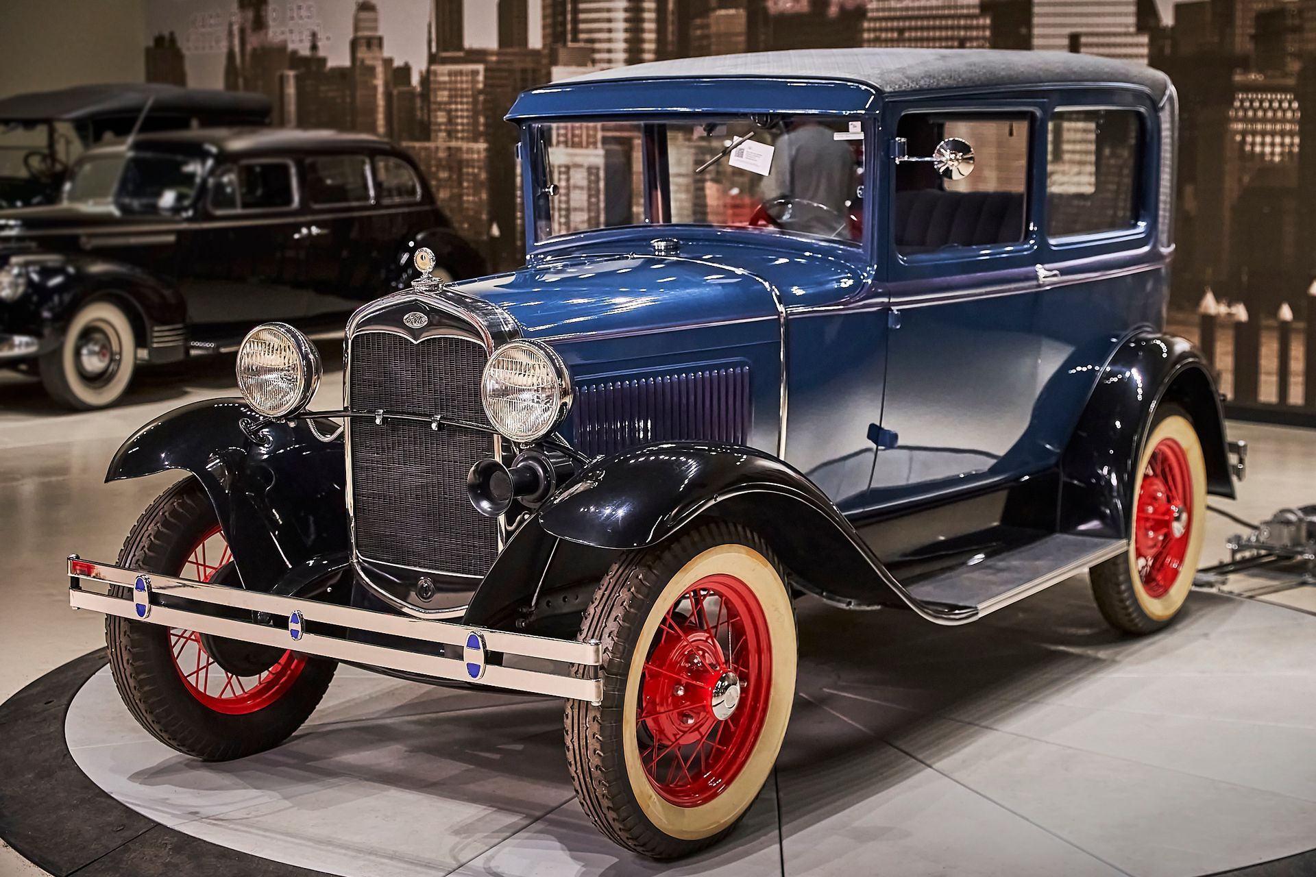 An old blue car with red wheels is parked in a garage.