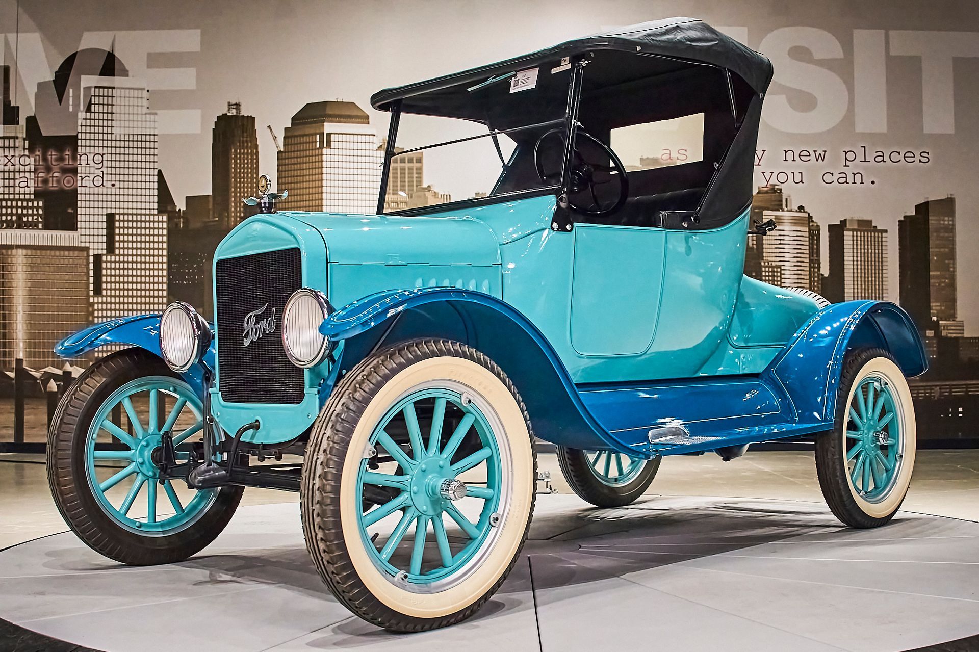 An old blue car is parked in front of a city skyline