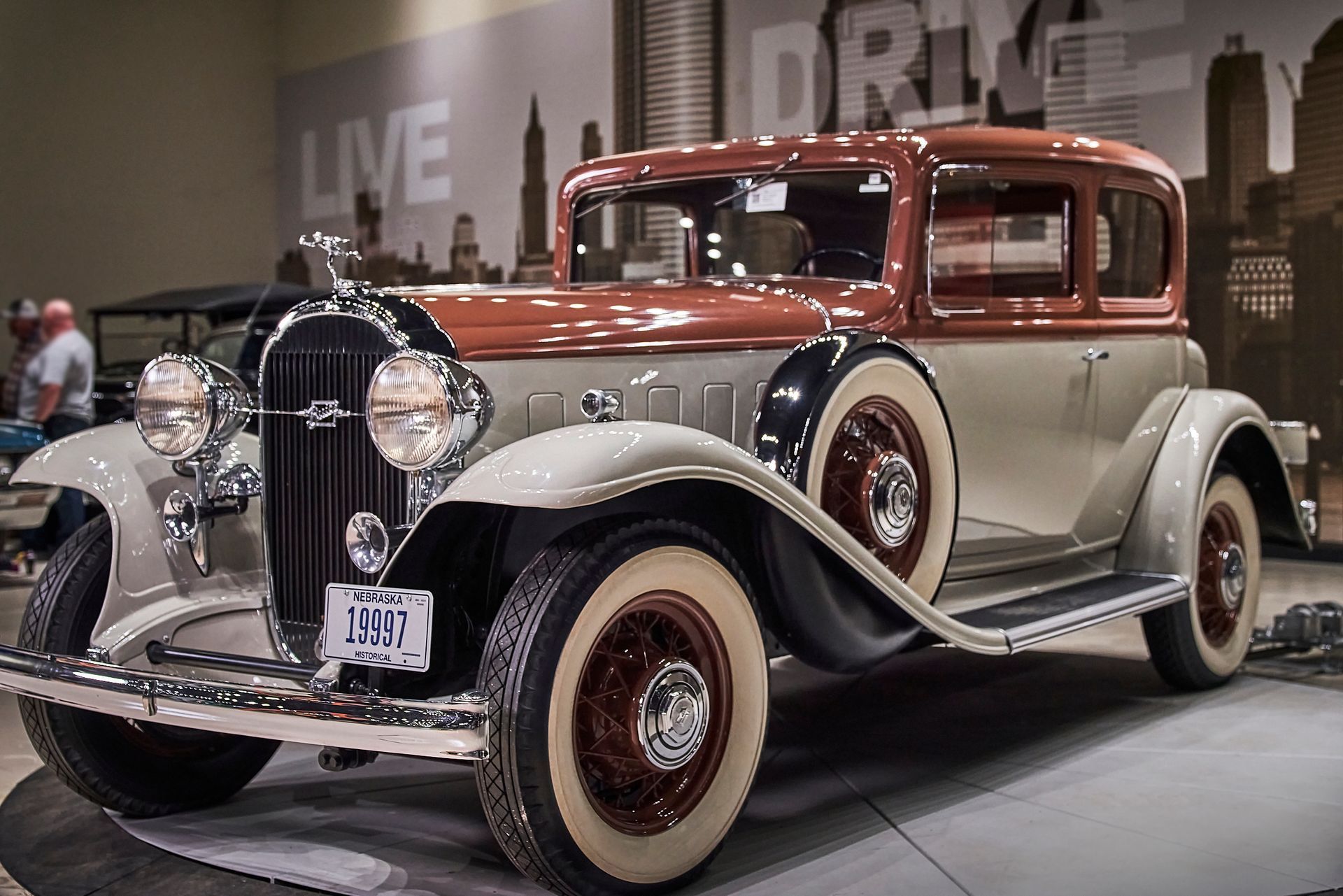 An old car is parked in front of a sign that says live drive