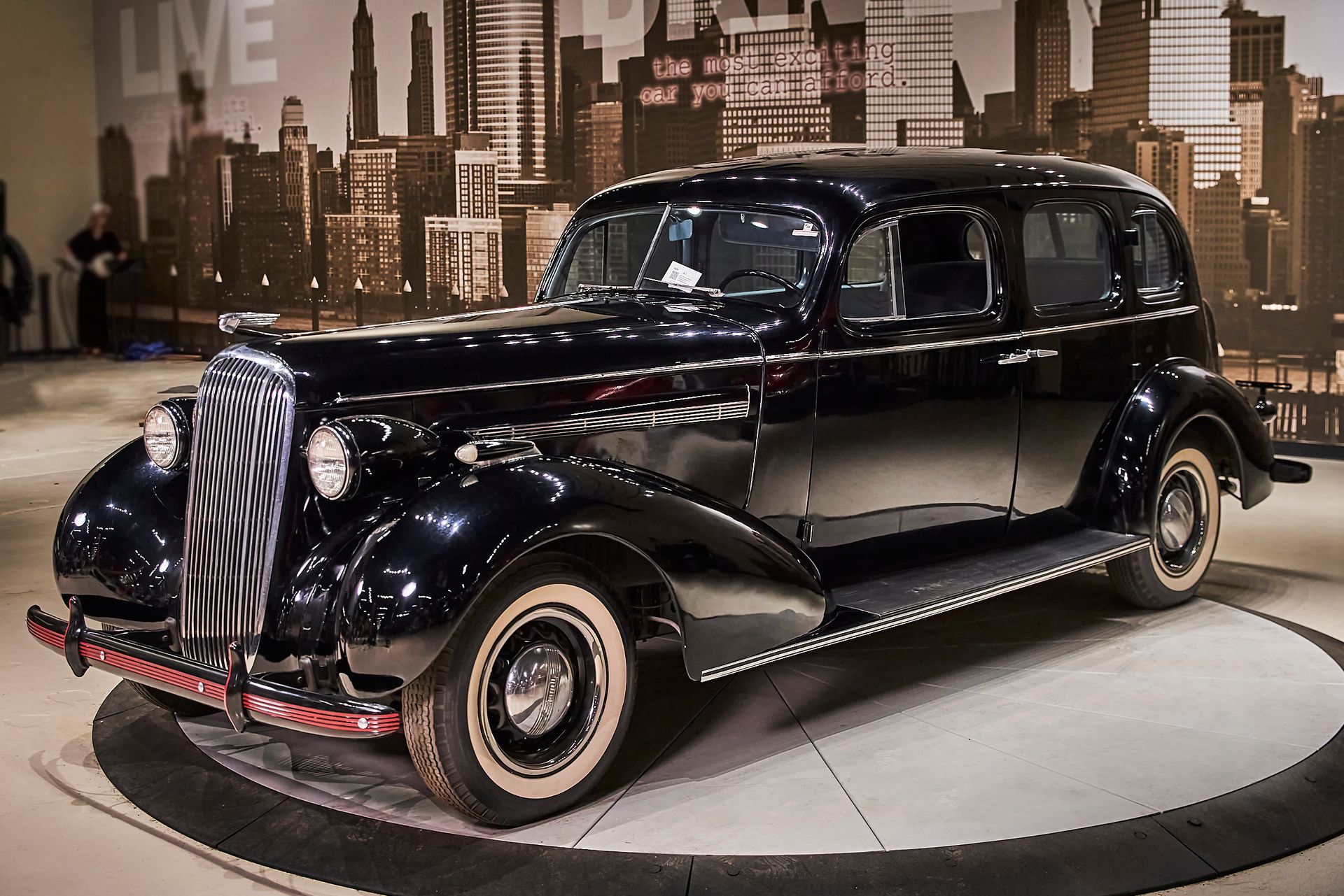 An old black car is on display in front of a city skyline