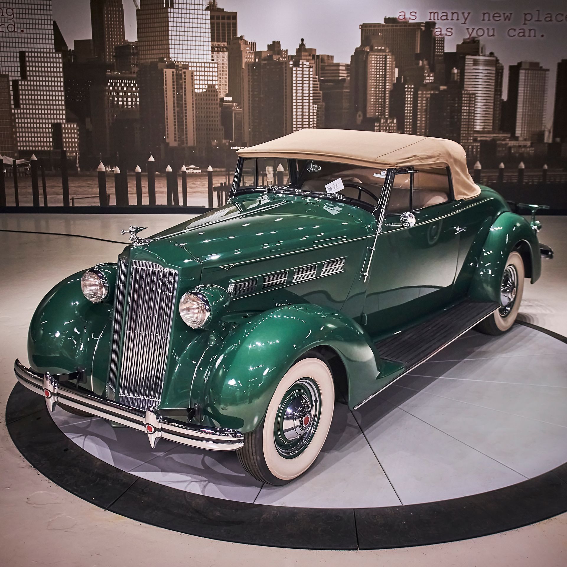 An old green car is on display in front of a city skyline