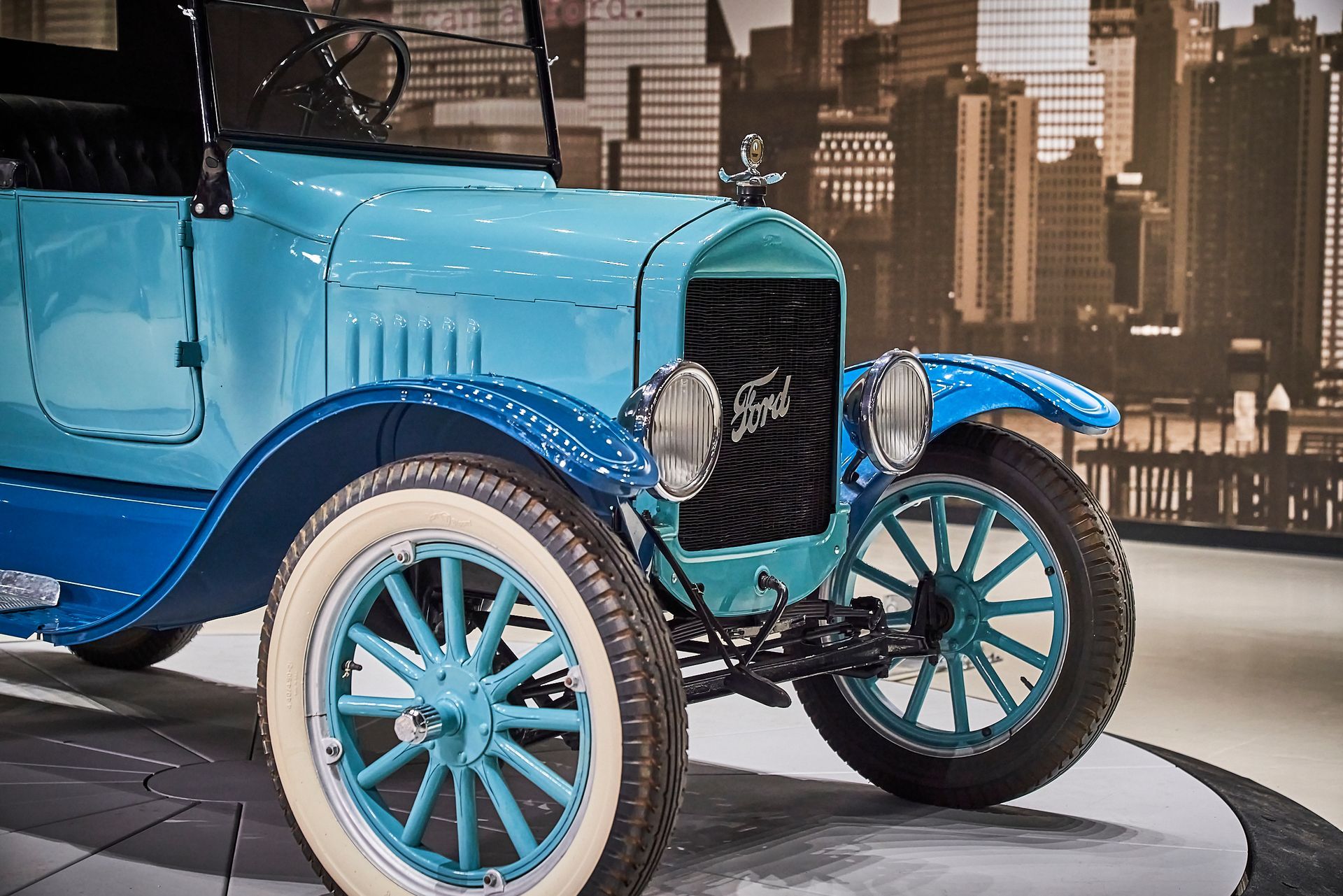 A blue ford car is parked in front of a city skyline