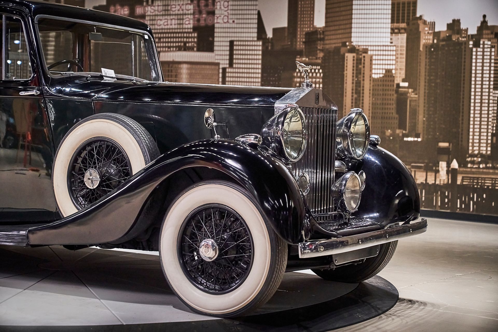 A black car with white tires is parked in front of a city skyline