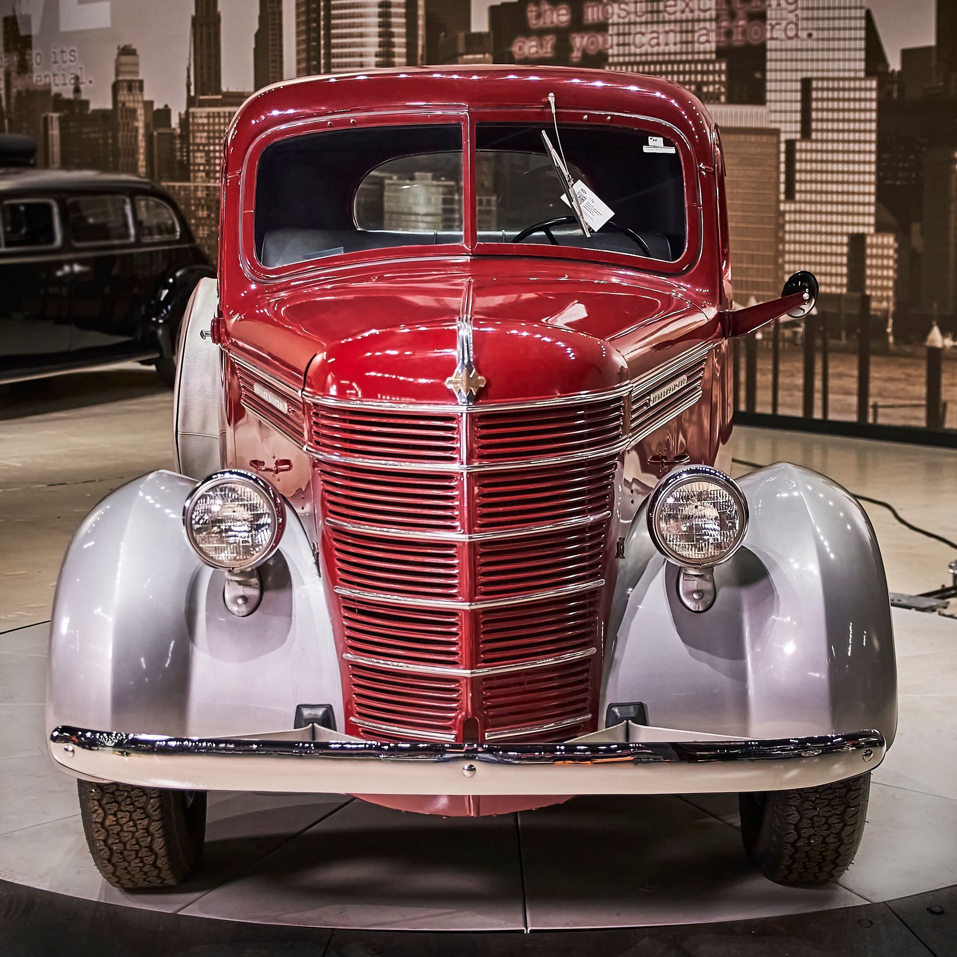 A red car is parked in front of a city skyline