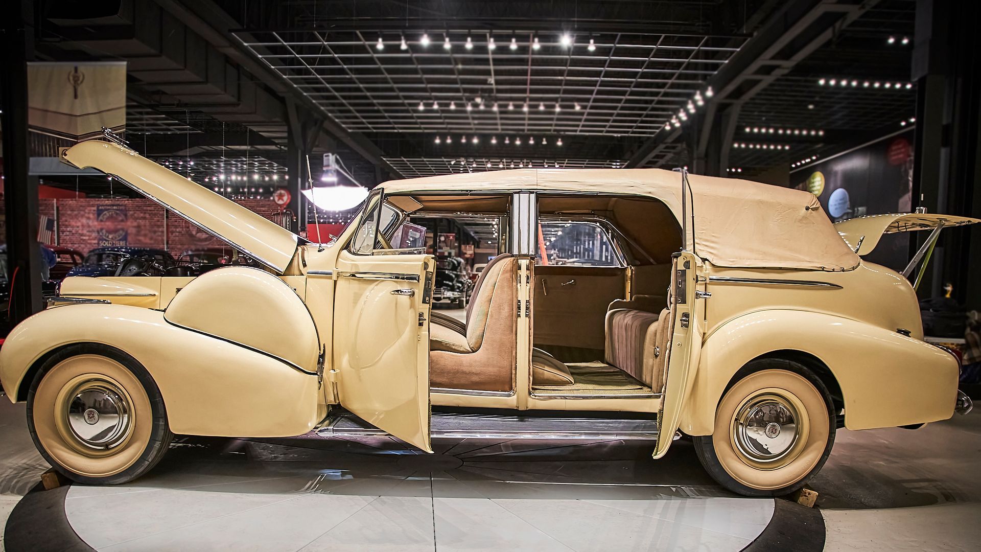 An old car with its hood open is sitting in a garage.
