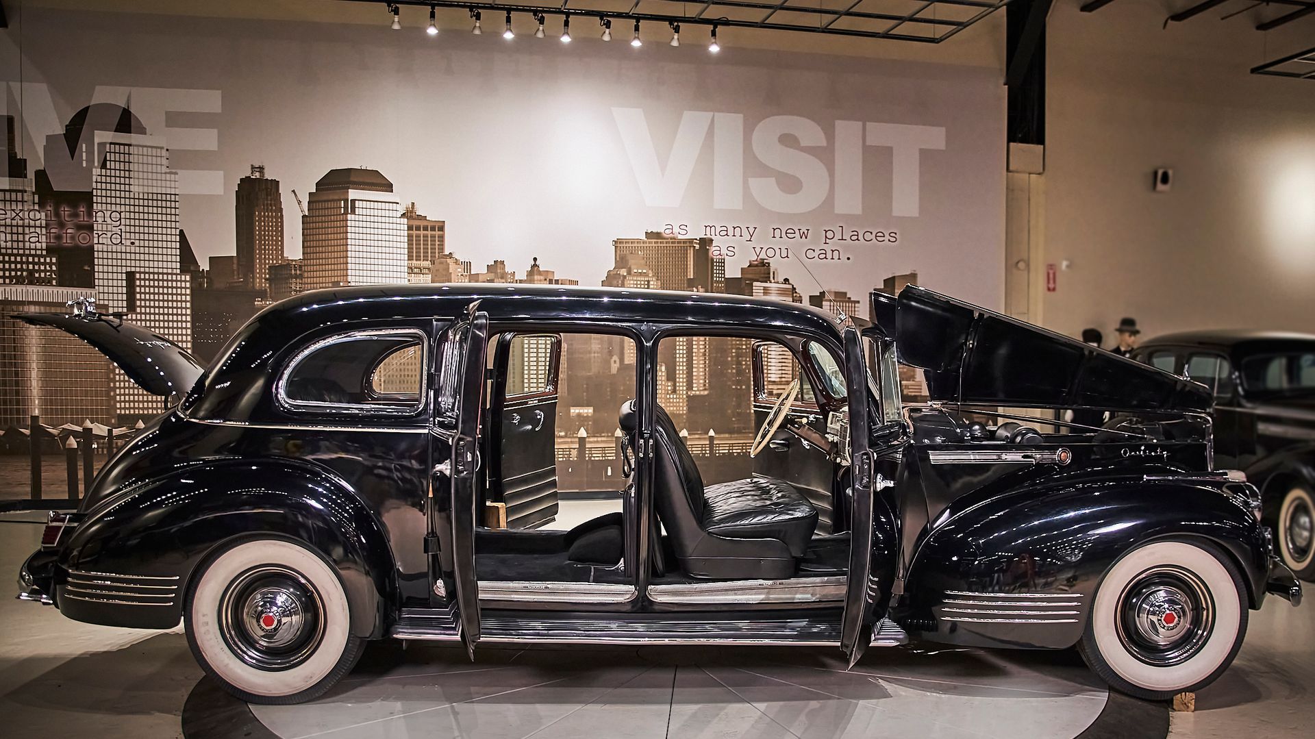 A black car is parked in front of a wall that says visit