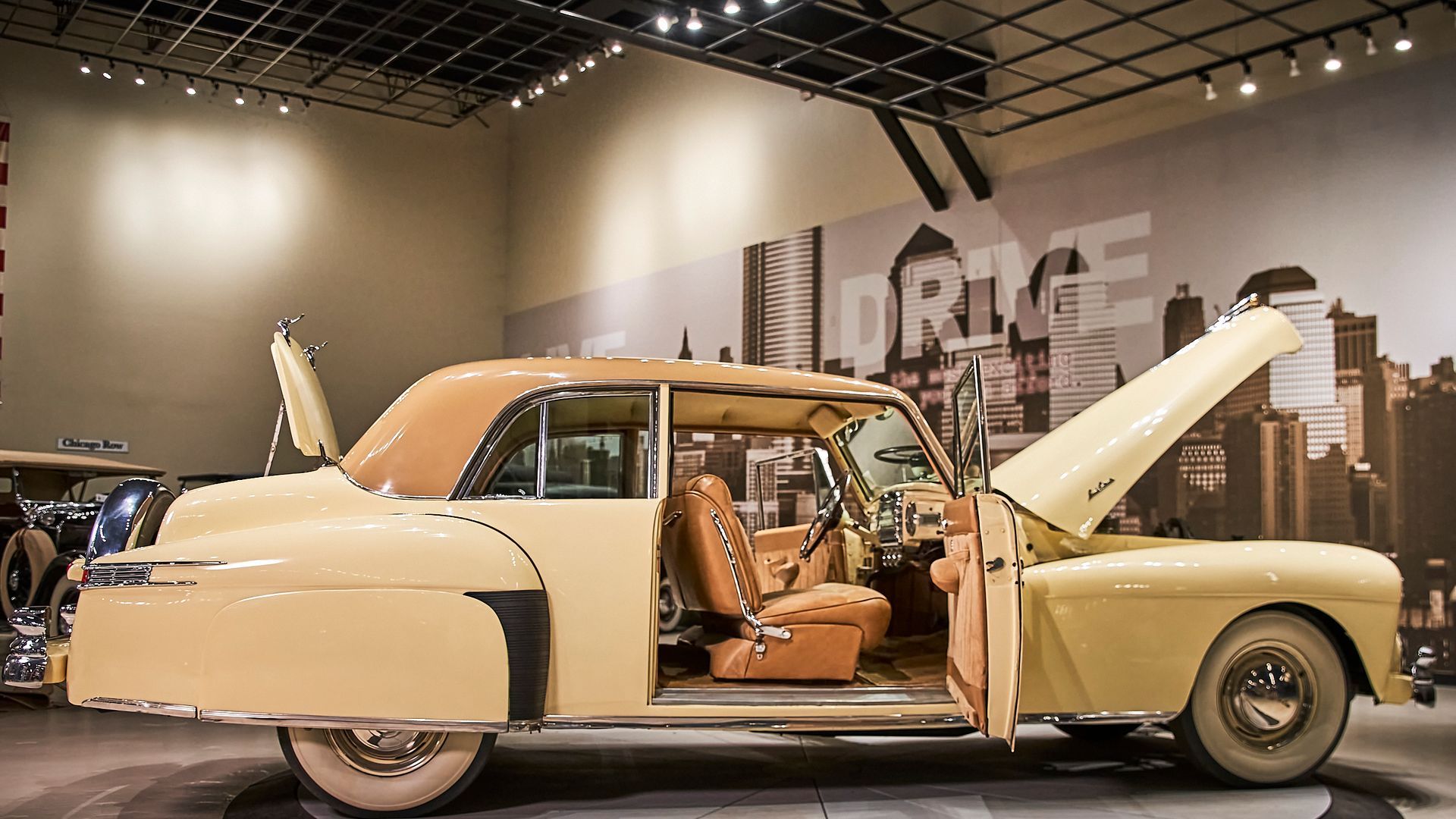 An old car is parked in a museum with its hood up.