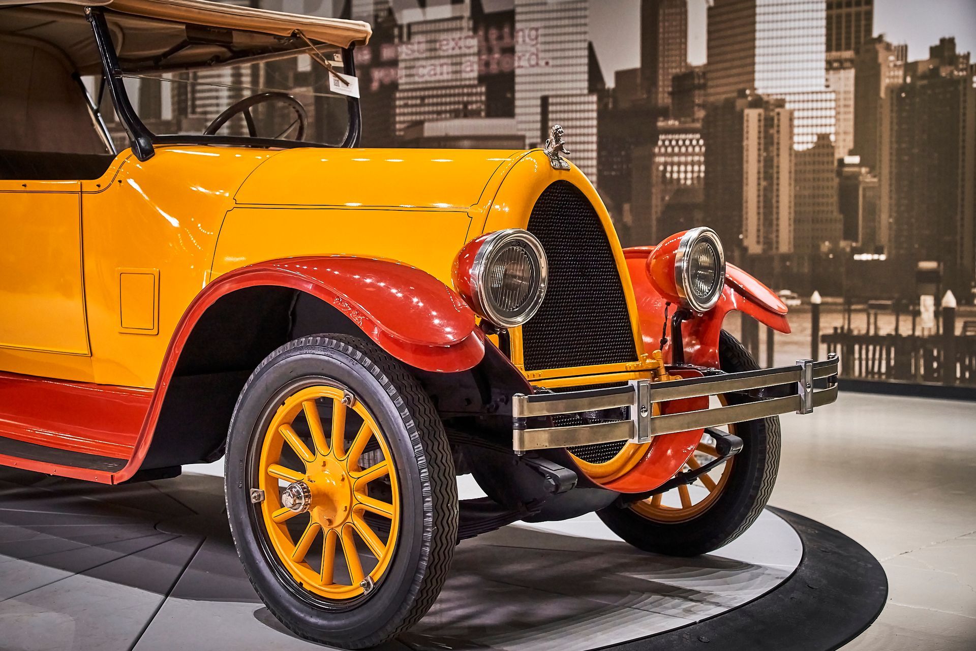 An old yellow and red car is parked in front of a city skyline.