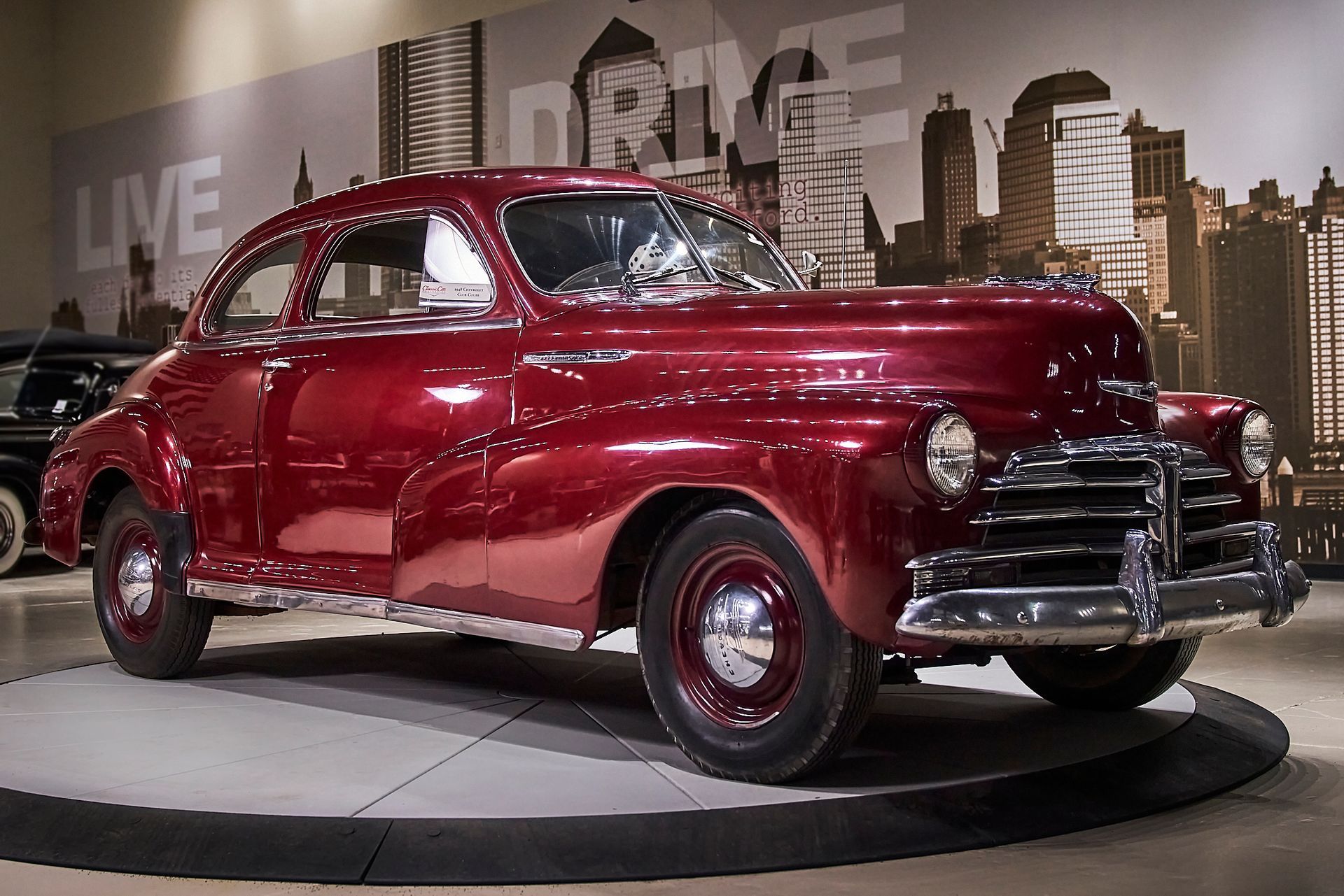 A red car is on display in front of a sign that says live drive