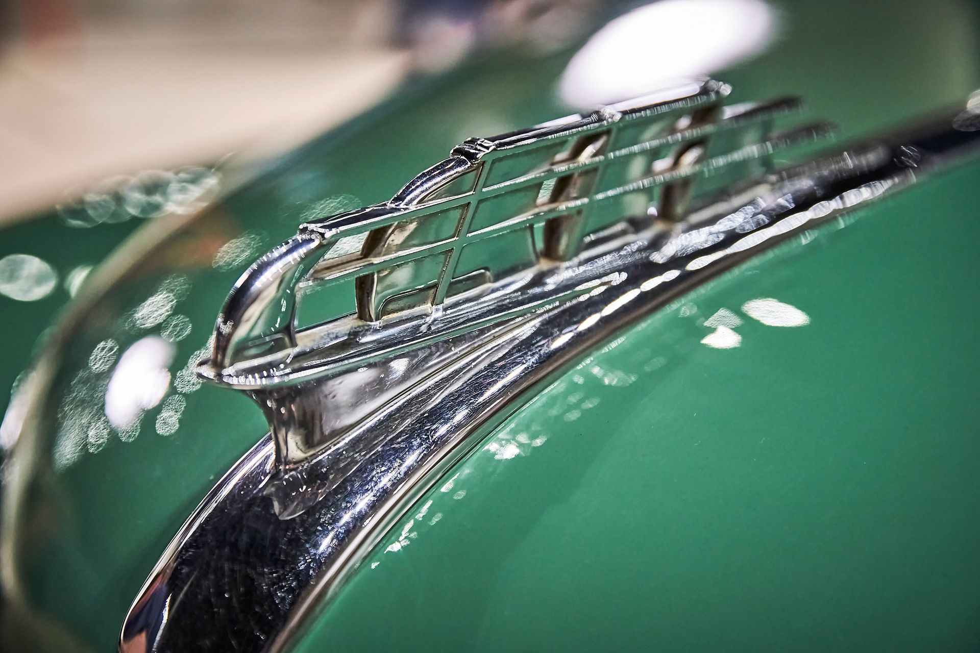 A close up of a green car with a chrome hood ornament.