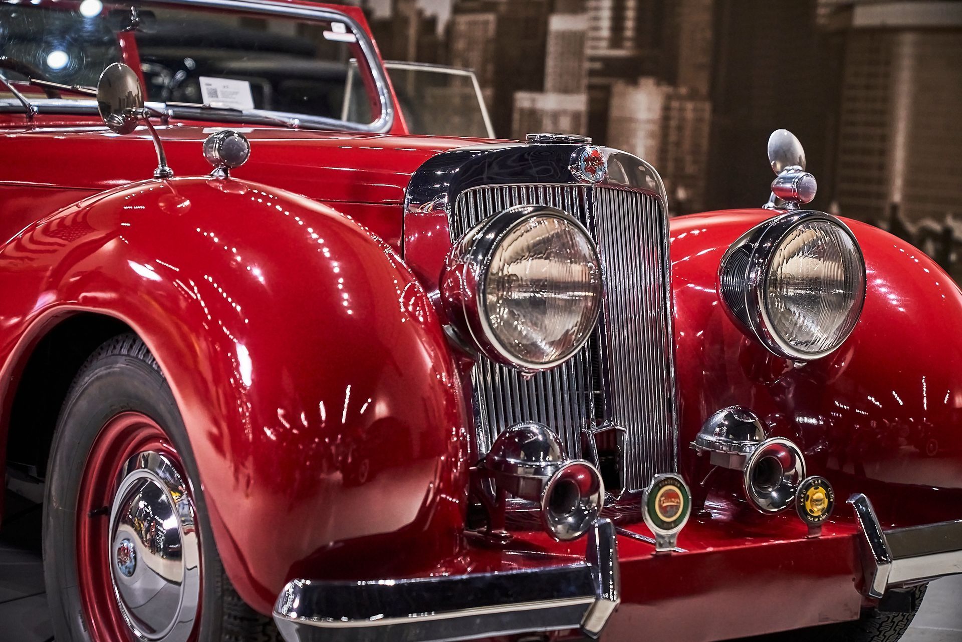 A red vintage car is parked in front of a city skyline.