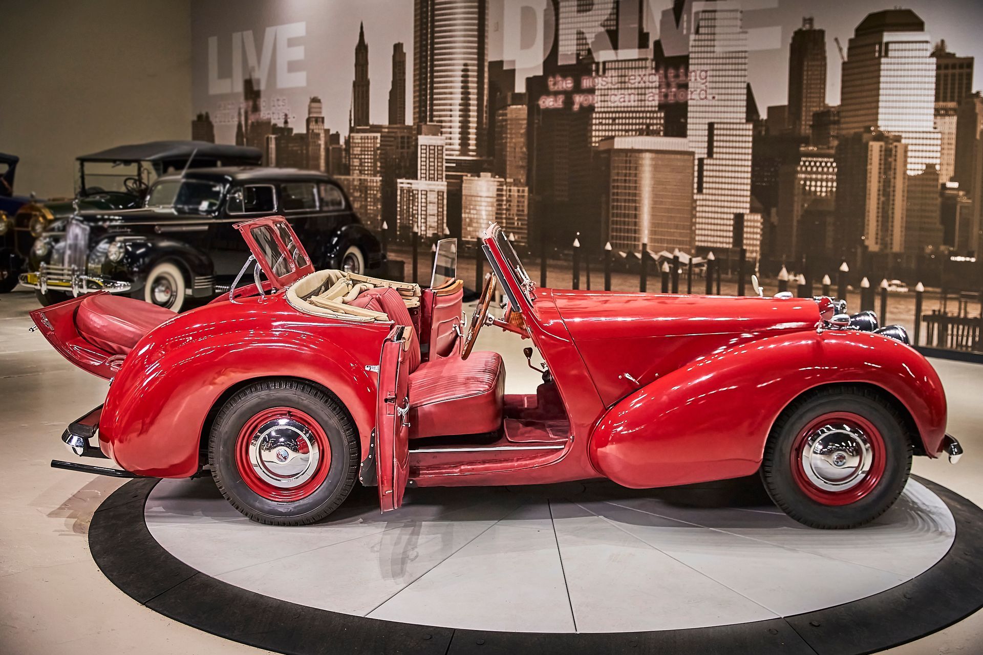 A red car is parked in front of a wall that says live and drive