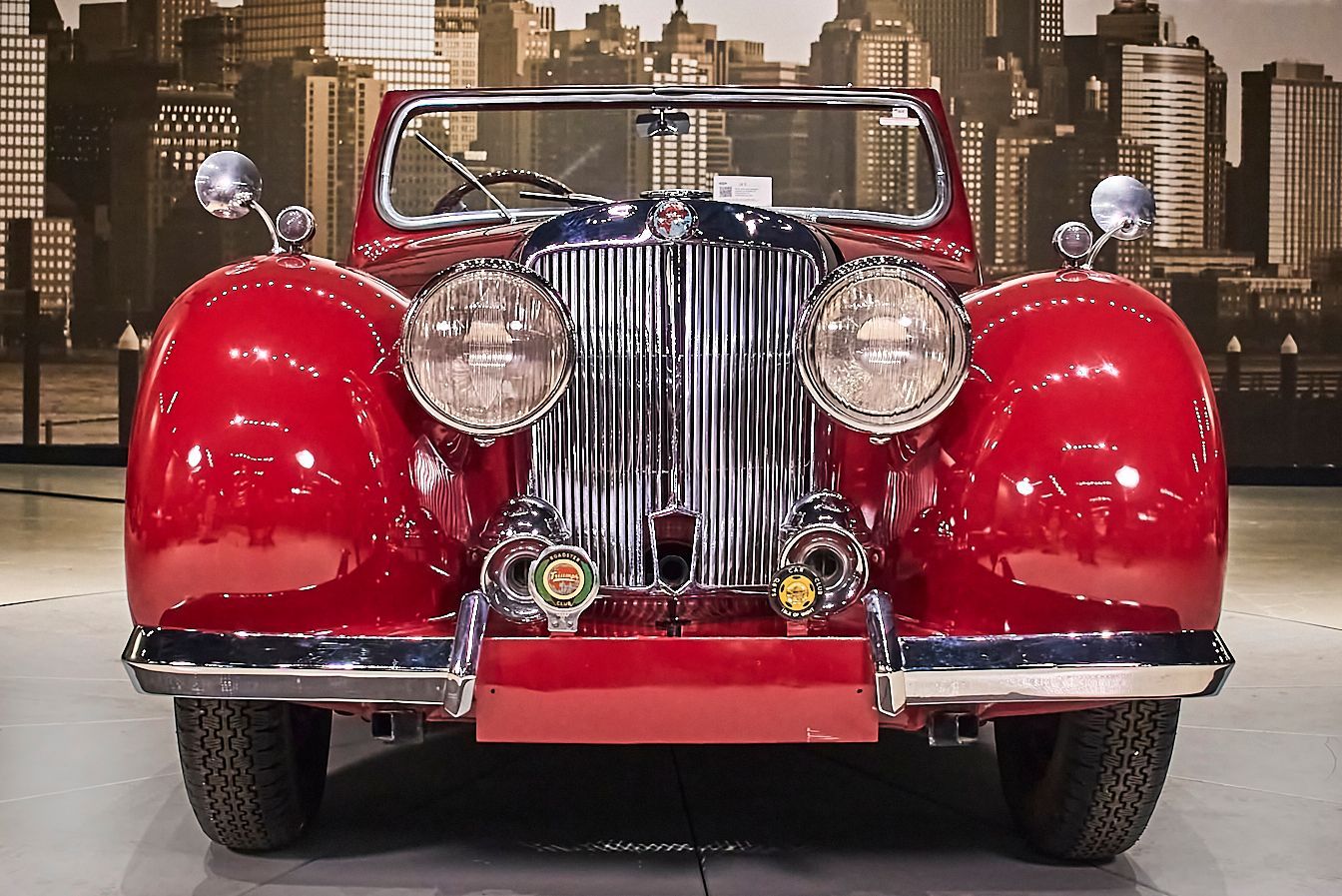 A red car is parked in front of a city skyline.