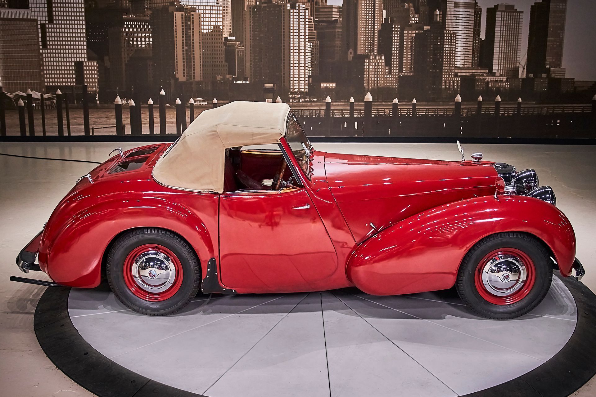 A red car is parked in front of a city skyline