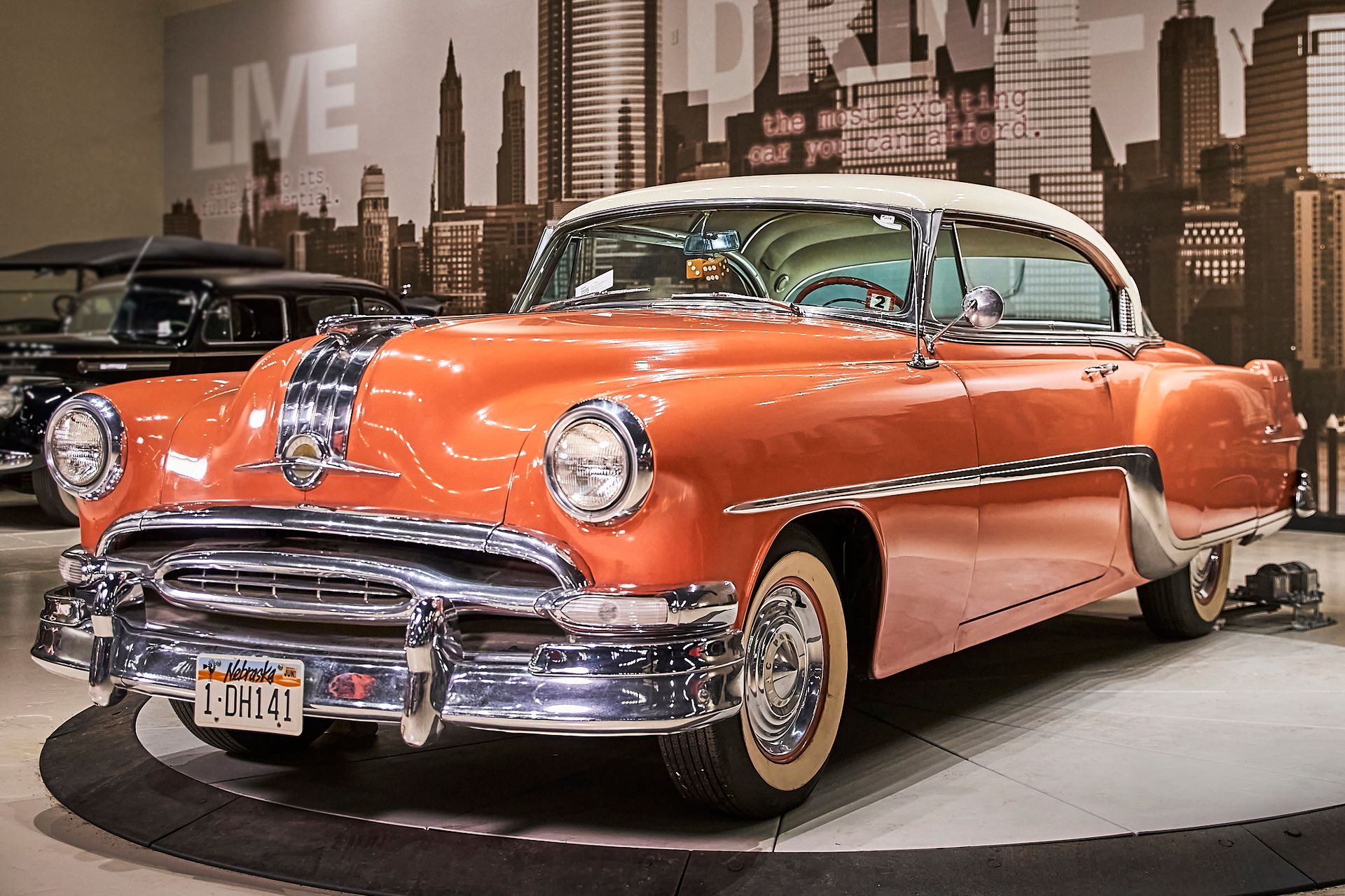 An old orange car is parked in front of a city skyline.