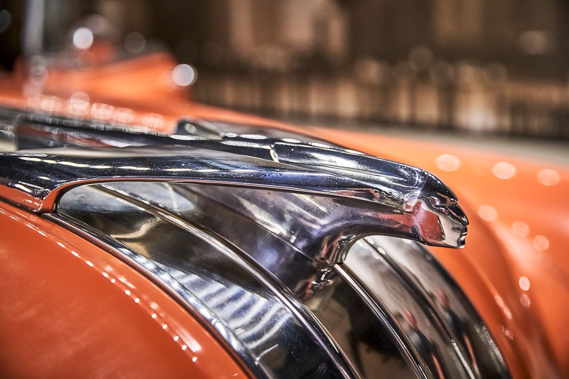 A close up of a chrome hood ornament on an orange car.