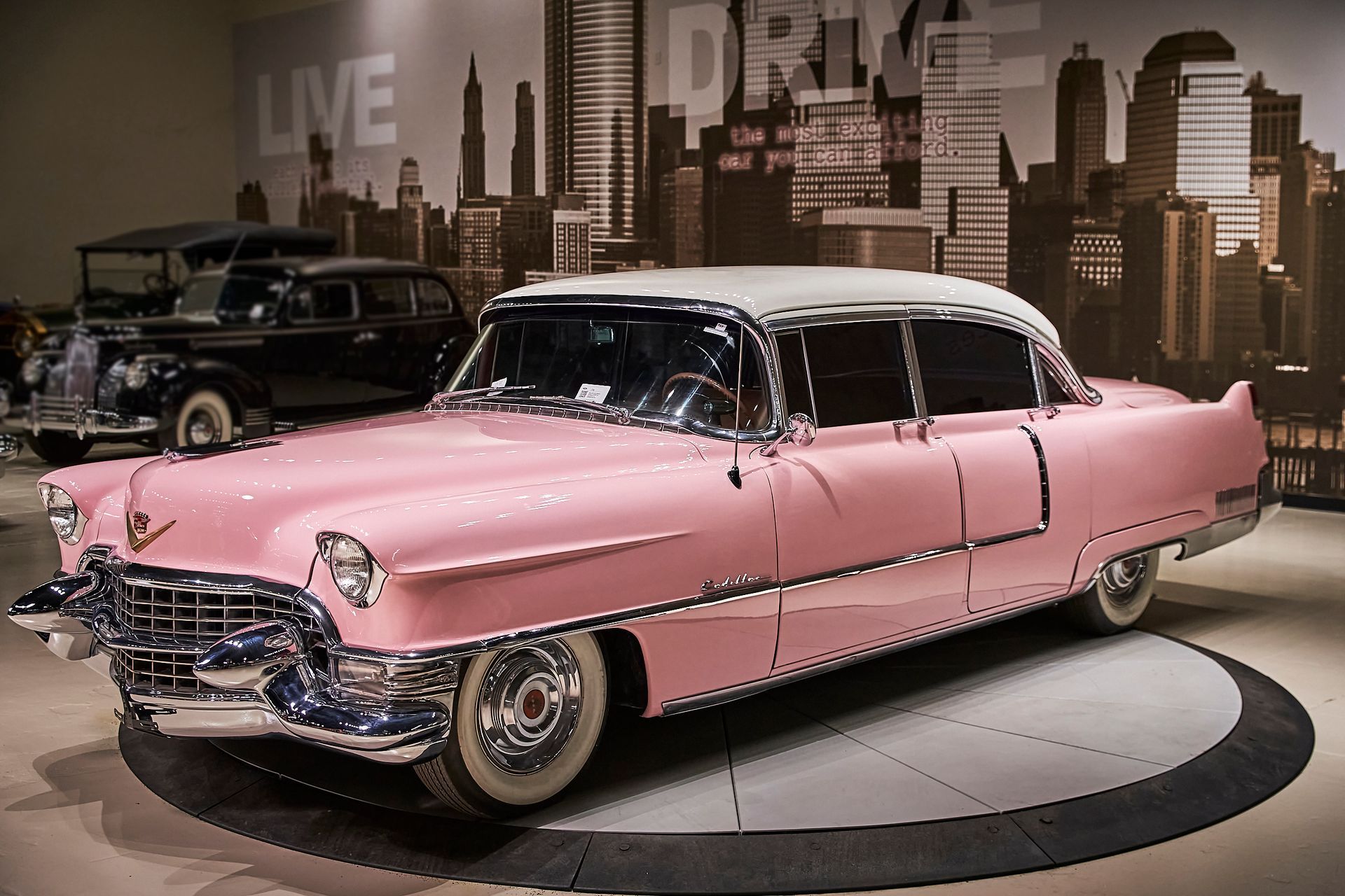A pink car is parked in front of a wall that says live on it