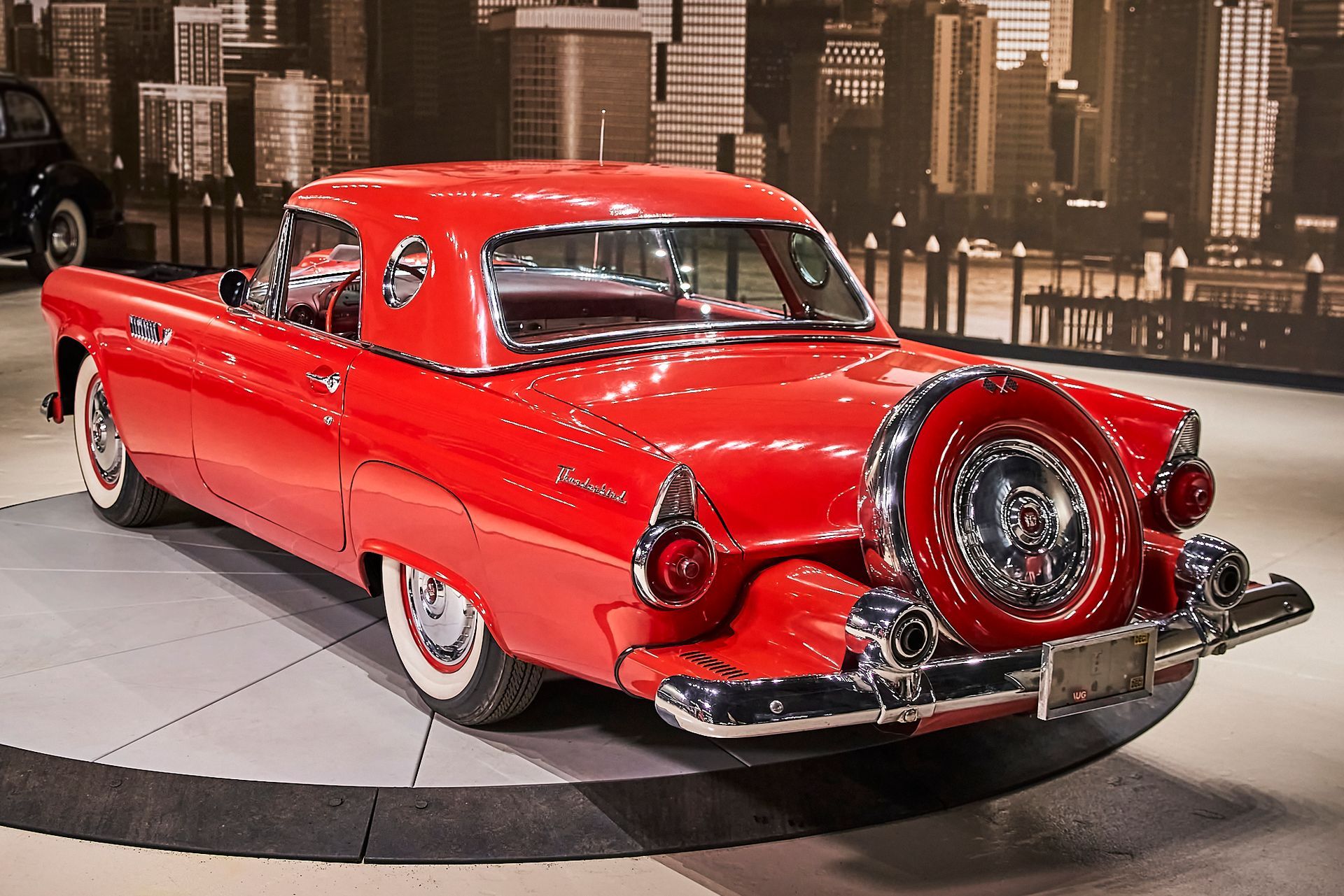 A red car is parked in front of a city skyline.