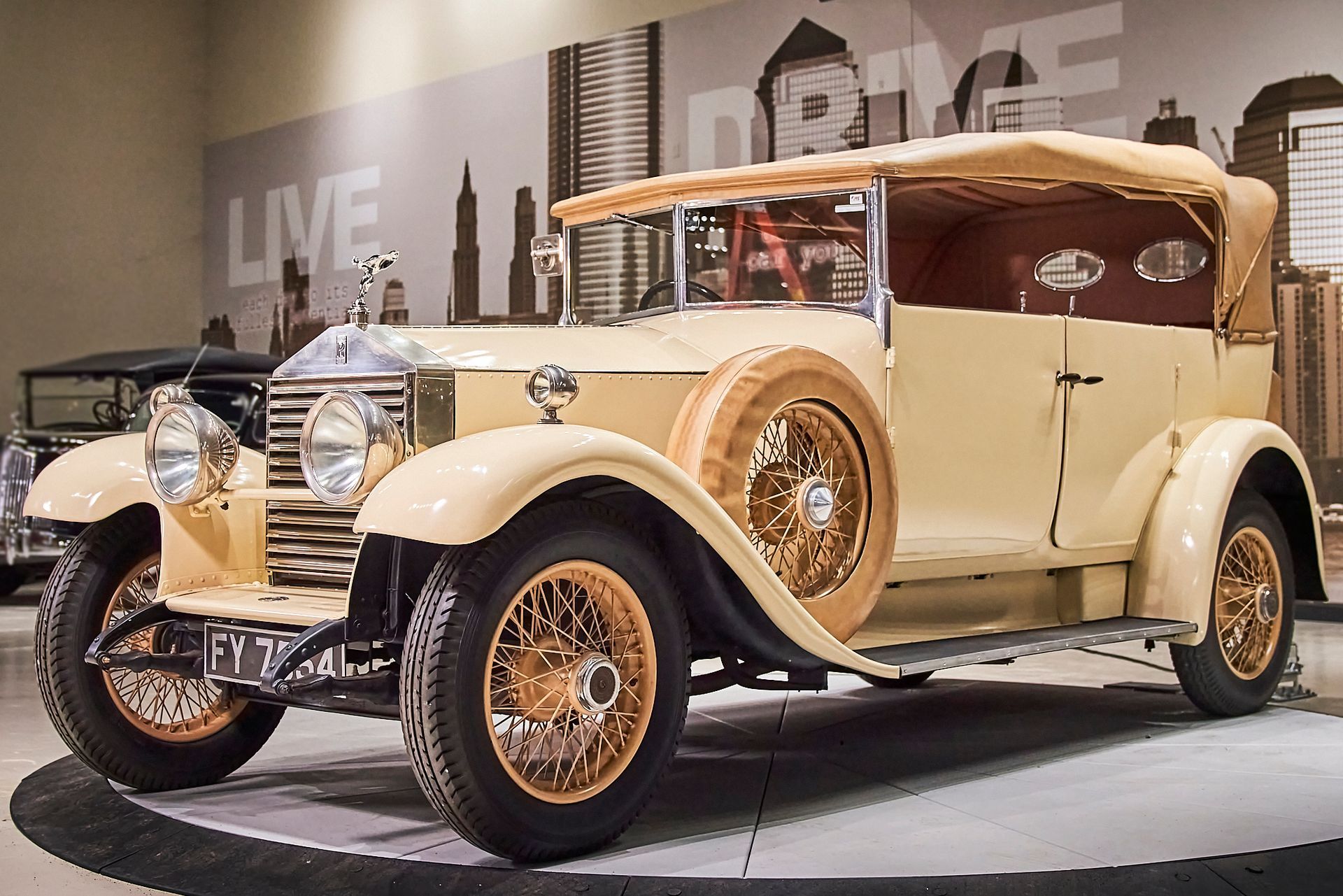 An old car is parked in front of a wall that says live drive