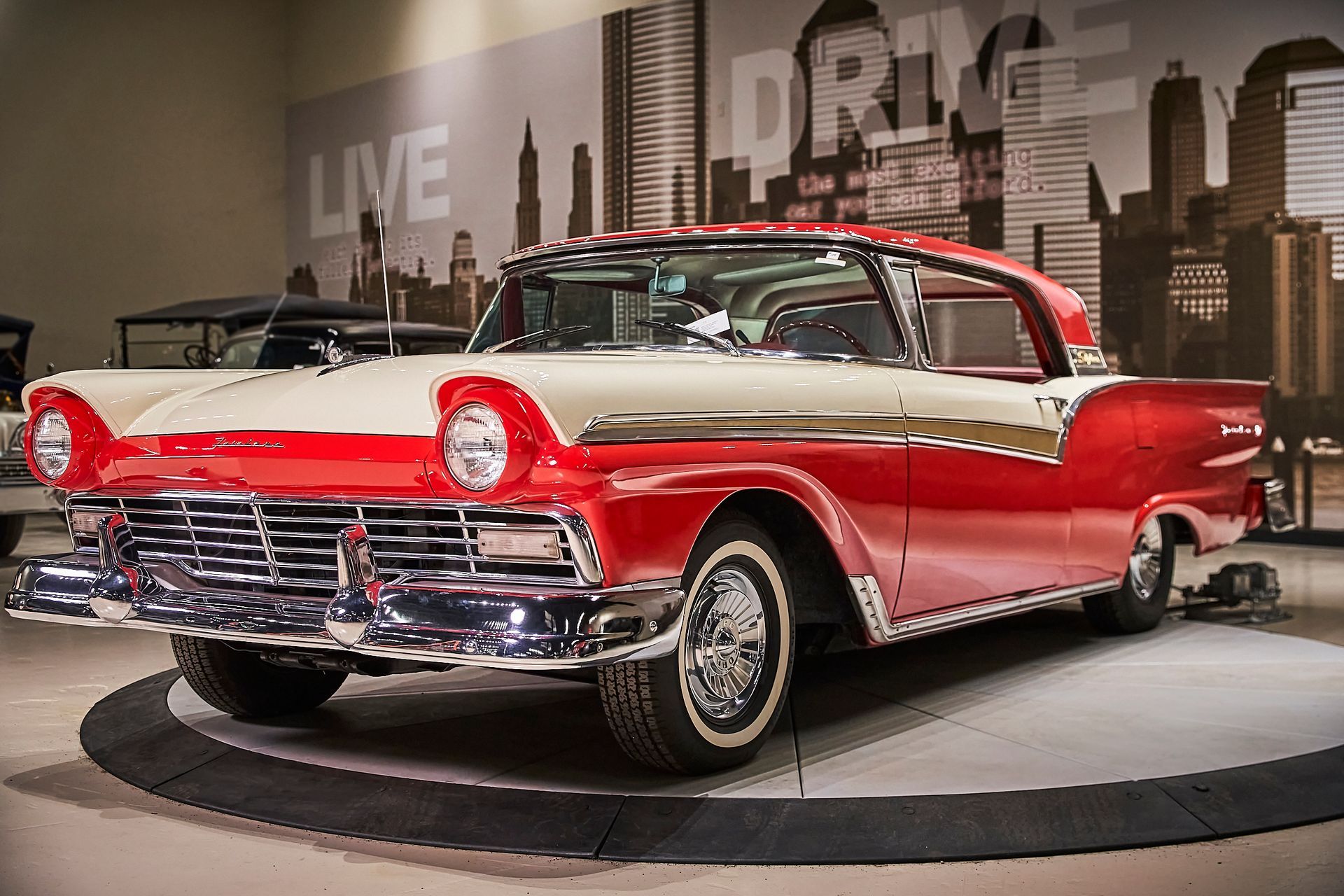 A red and white car is parked in front of a sign that says live drive