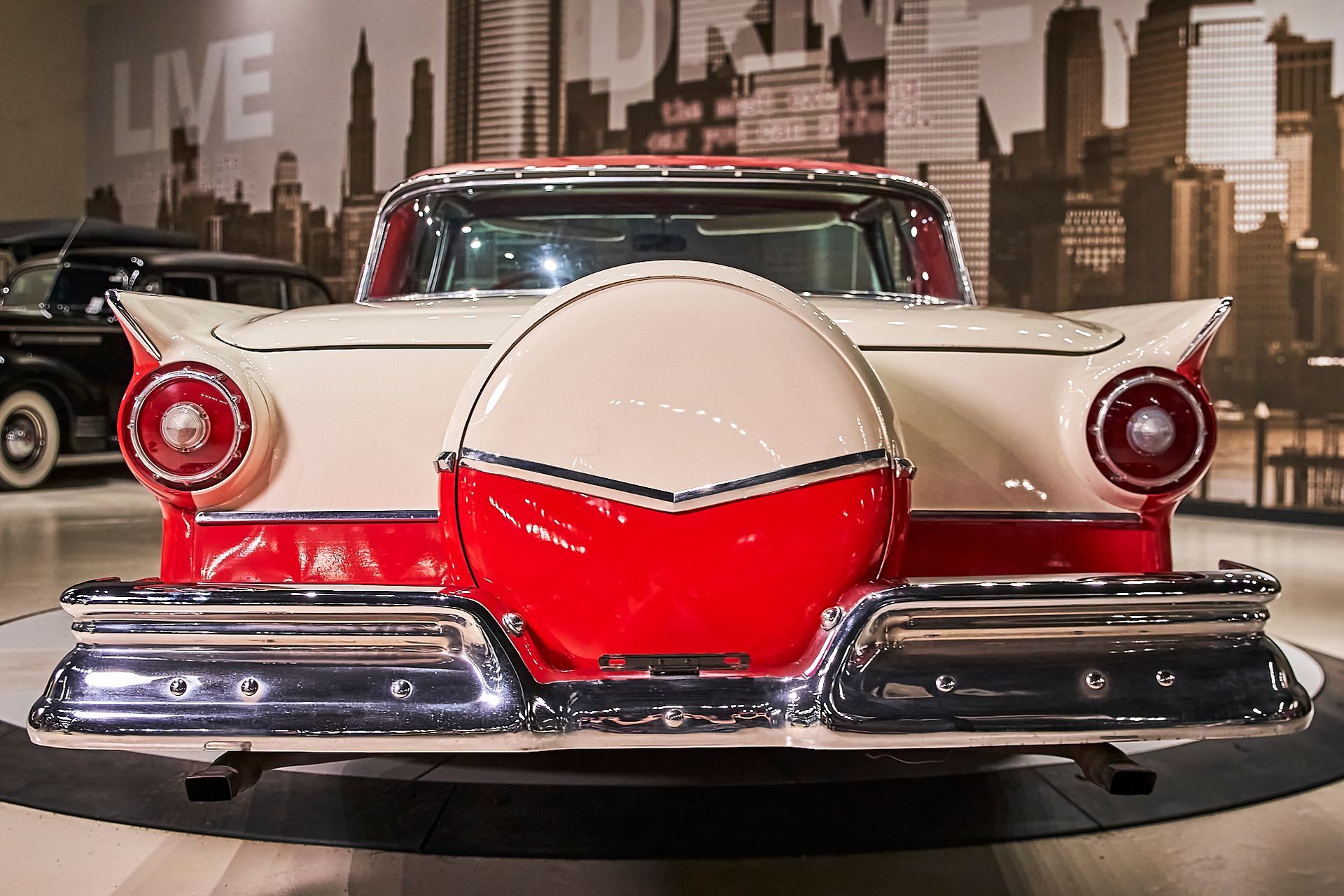A red and white car is parked in front of a city skyline.
