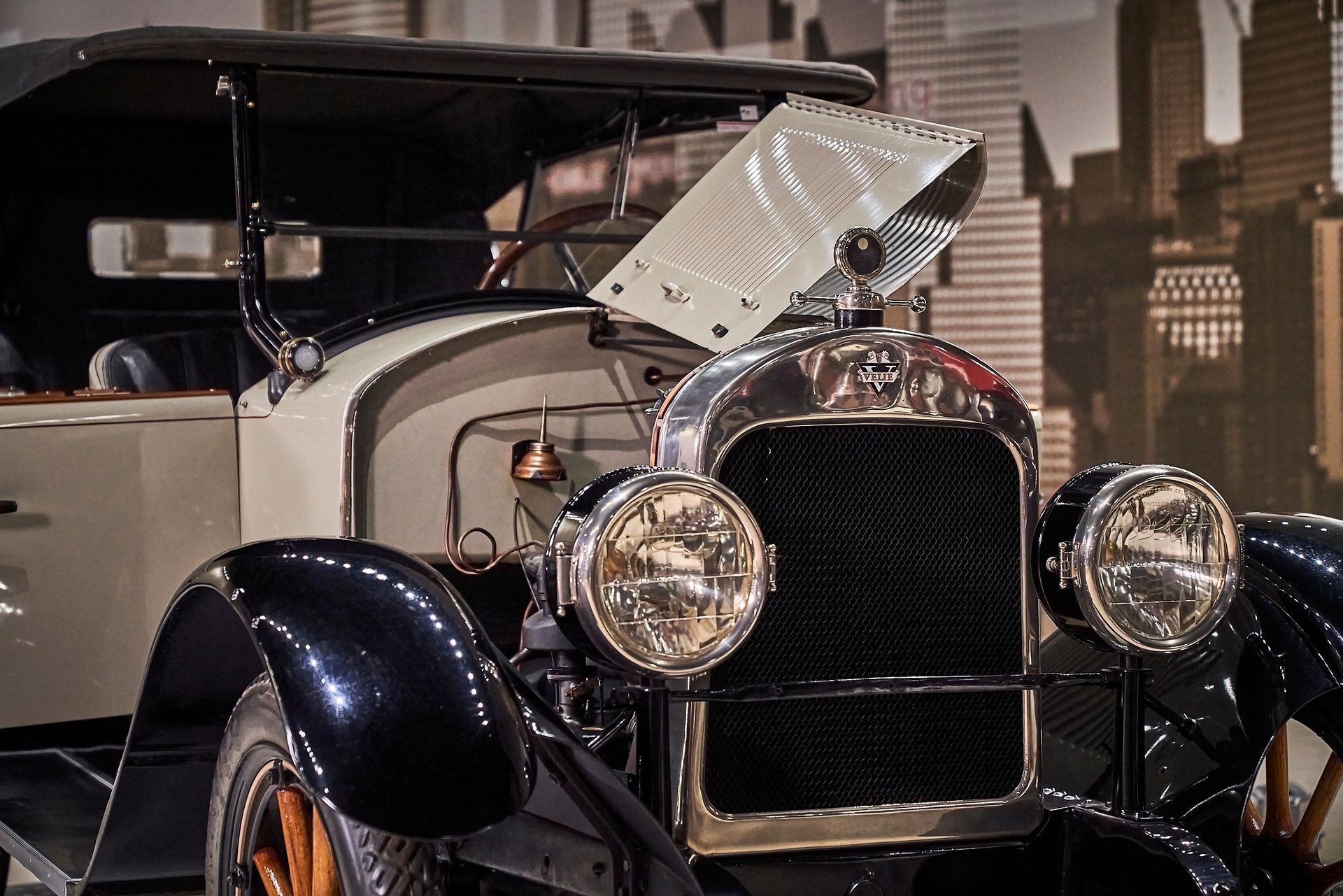 A black and white old car is parked in front of a city skyline.