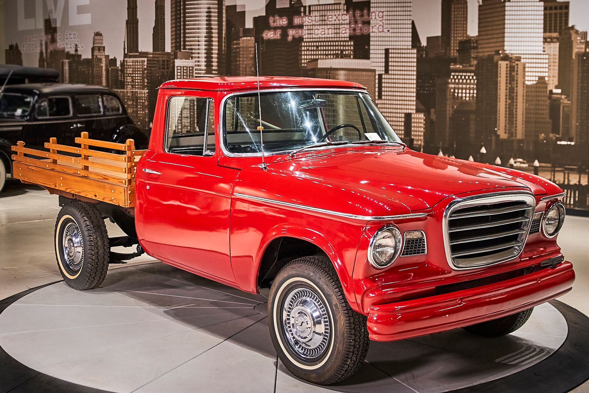 A red truck with a wooden bed is parked in front of a city skyline.