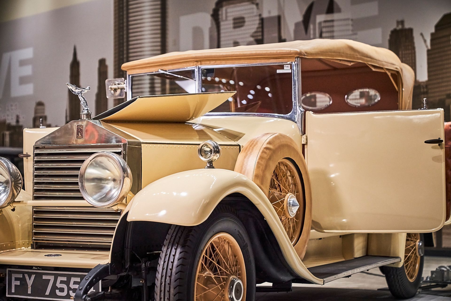 An old rolls royce car is parked in front of a city skyline.