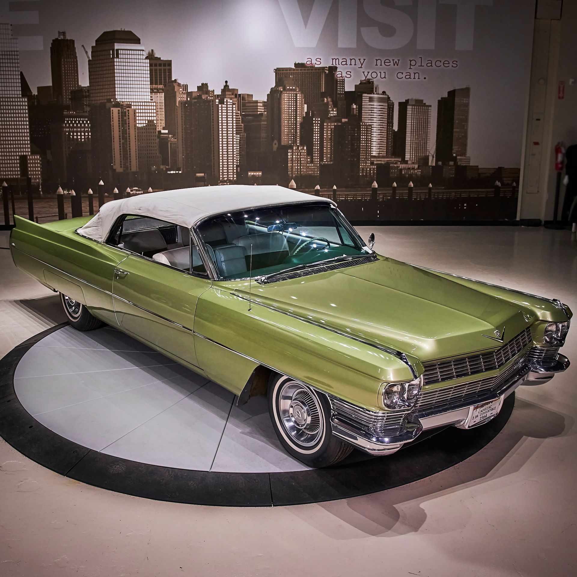 A green car is parked in front of a wall that says visit