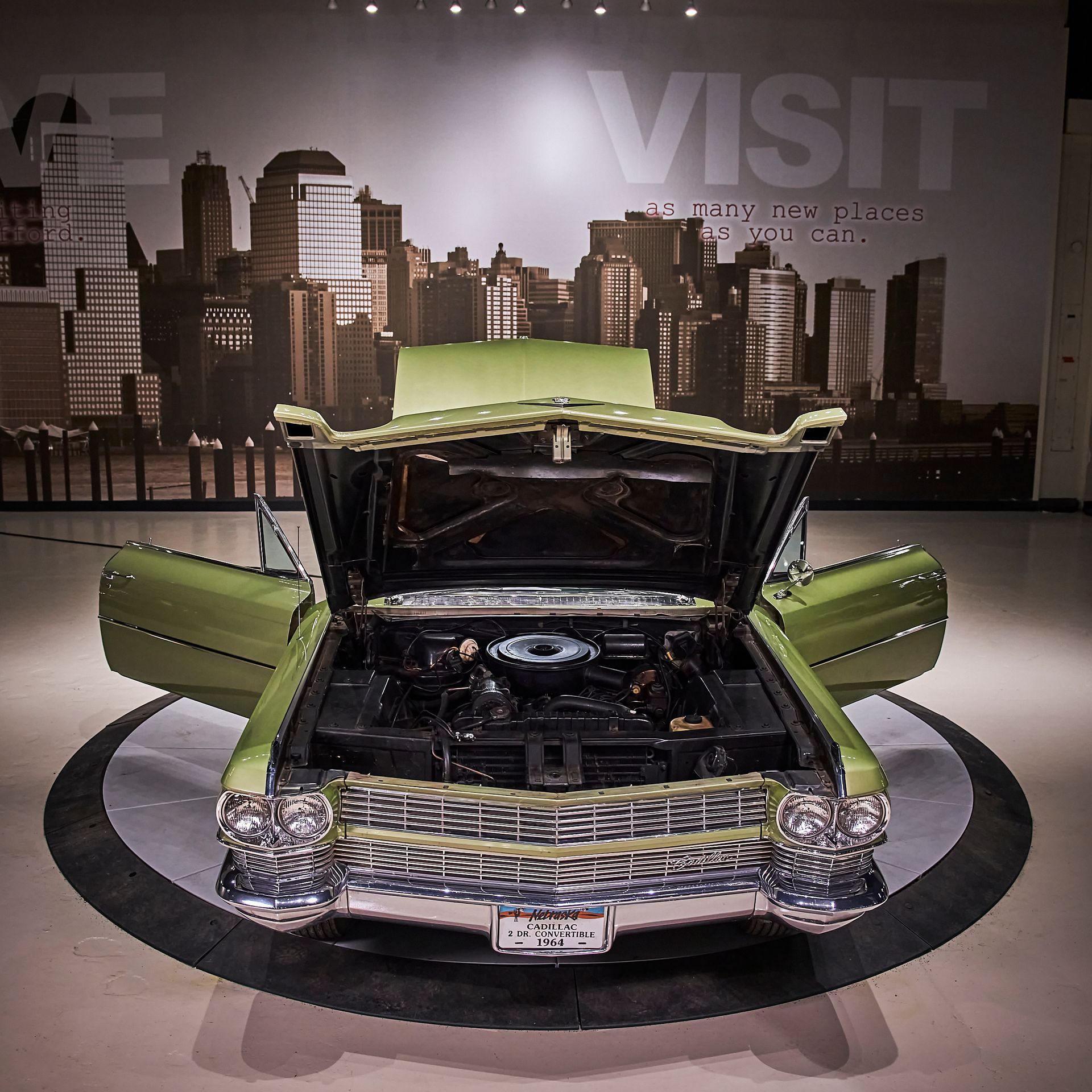 A green car with the hood open is in front of a wall that says visit